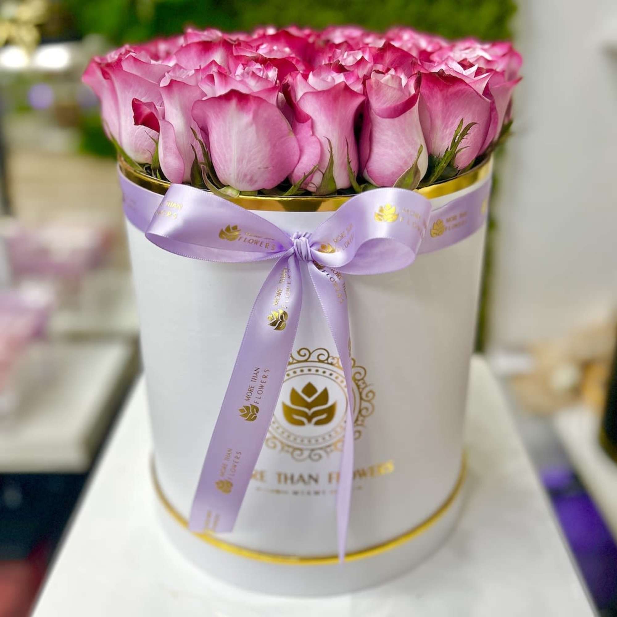Pink roses arranged tightly in a white hat box with a lavender ribbon bow