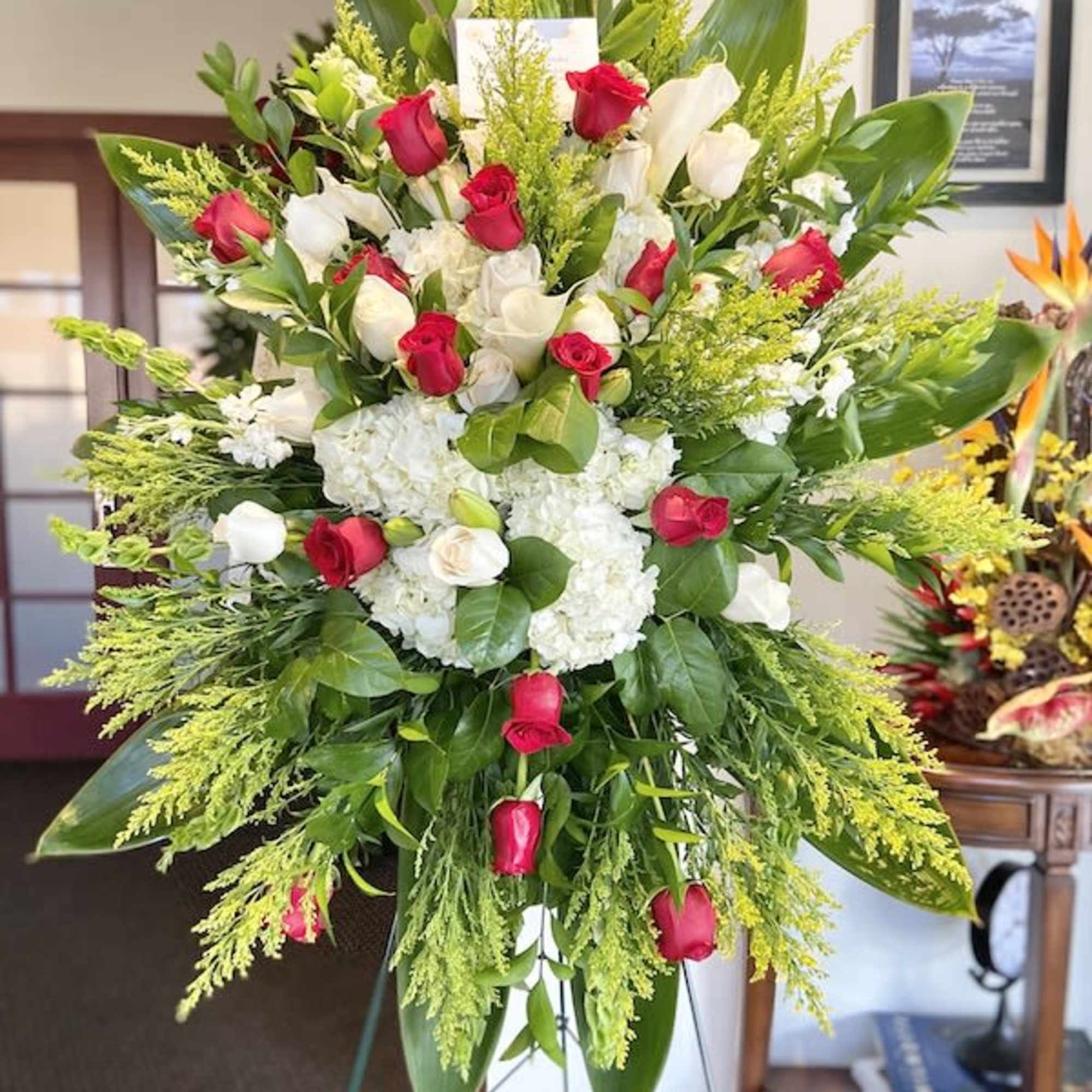 Tall standing spray of red and white roses with white hydrangeas on a green easel