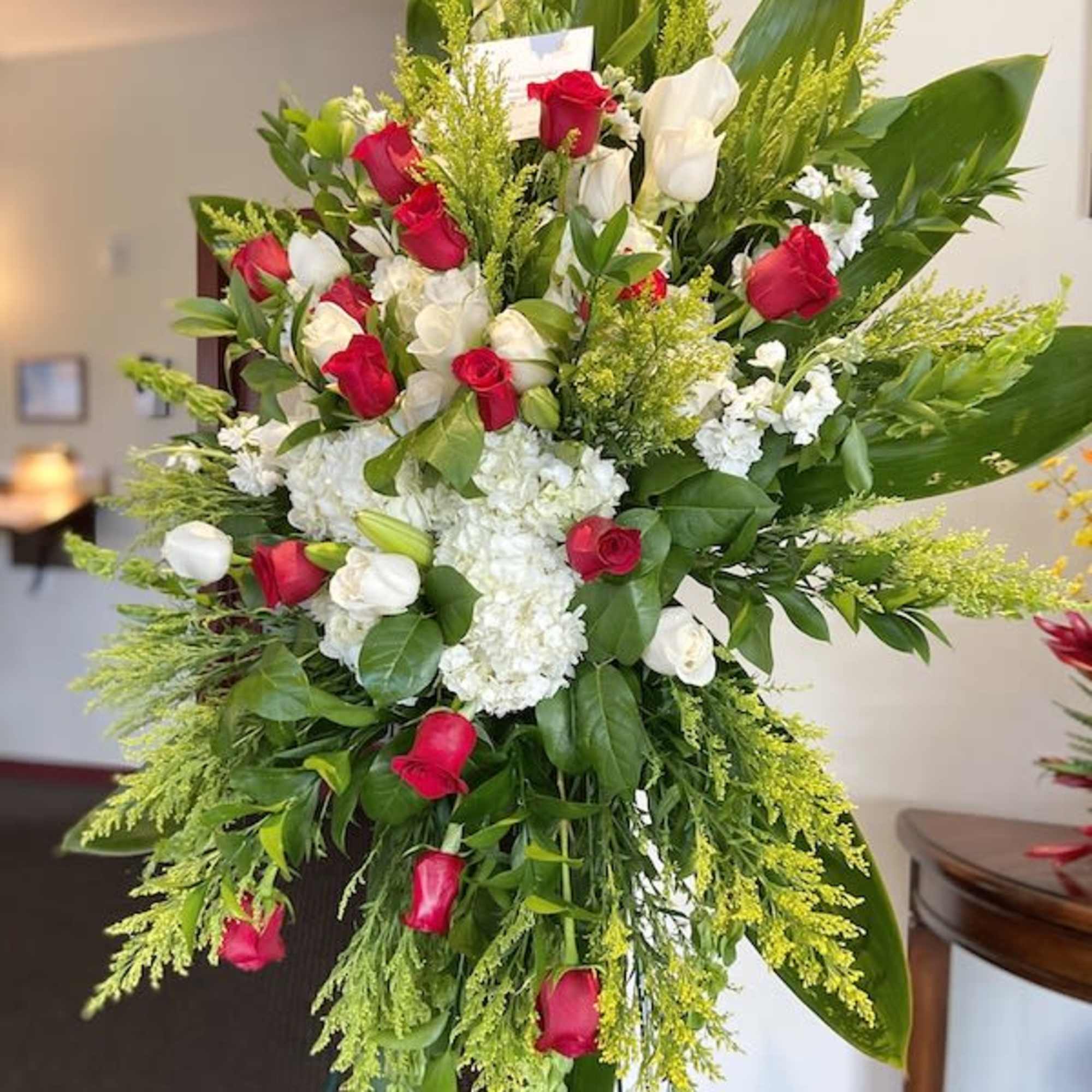 Tall standing spray of red roses, white calla lilies, and other white flowers on a metal easel.