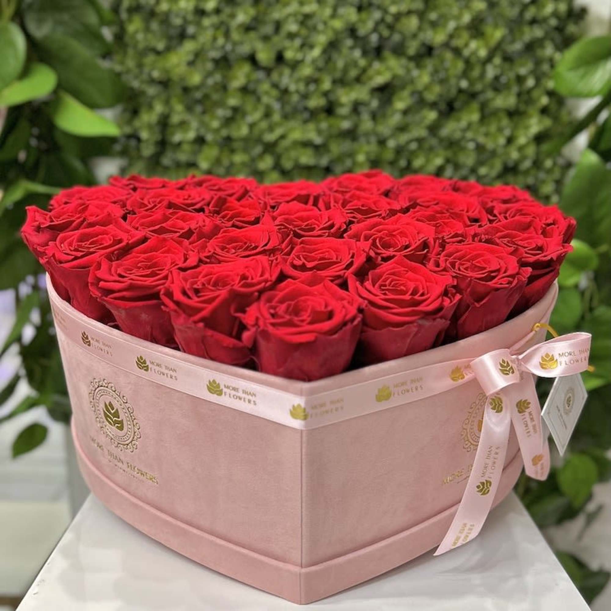 Heart-shaped pink box filled with red roses and tied with a pink ribbon.