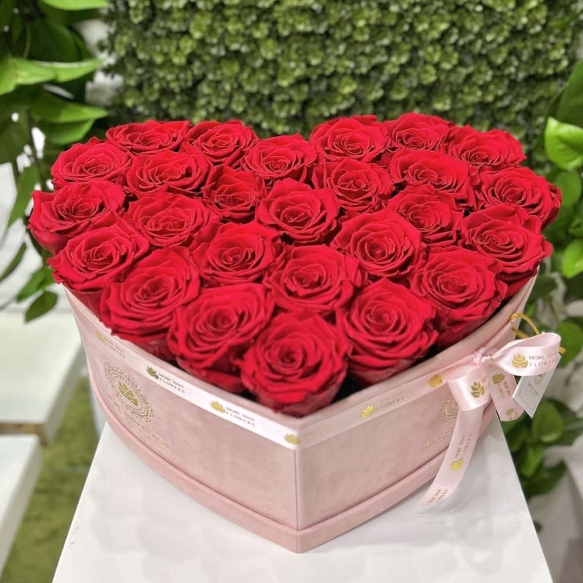 Heart-shaped pink box filled with tightly packed red roses on a white pedestal