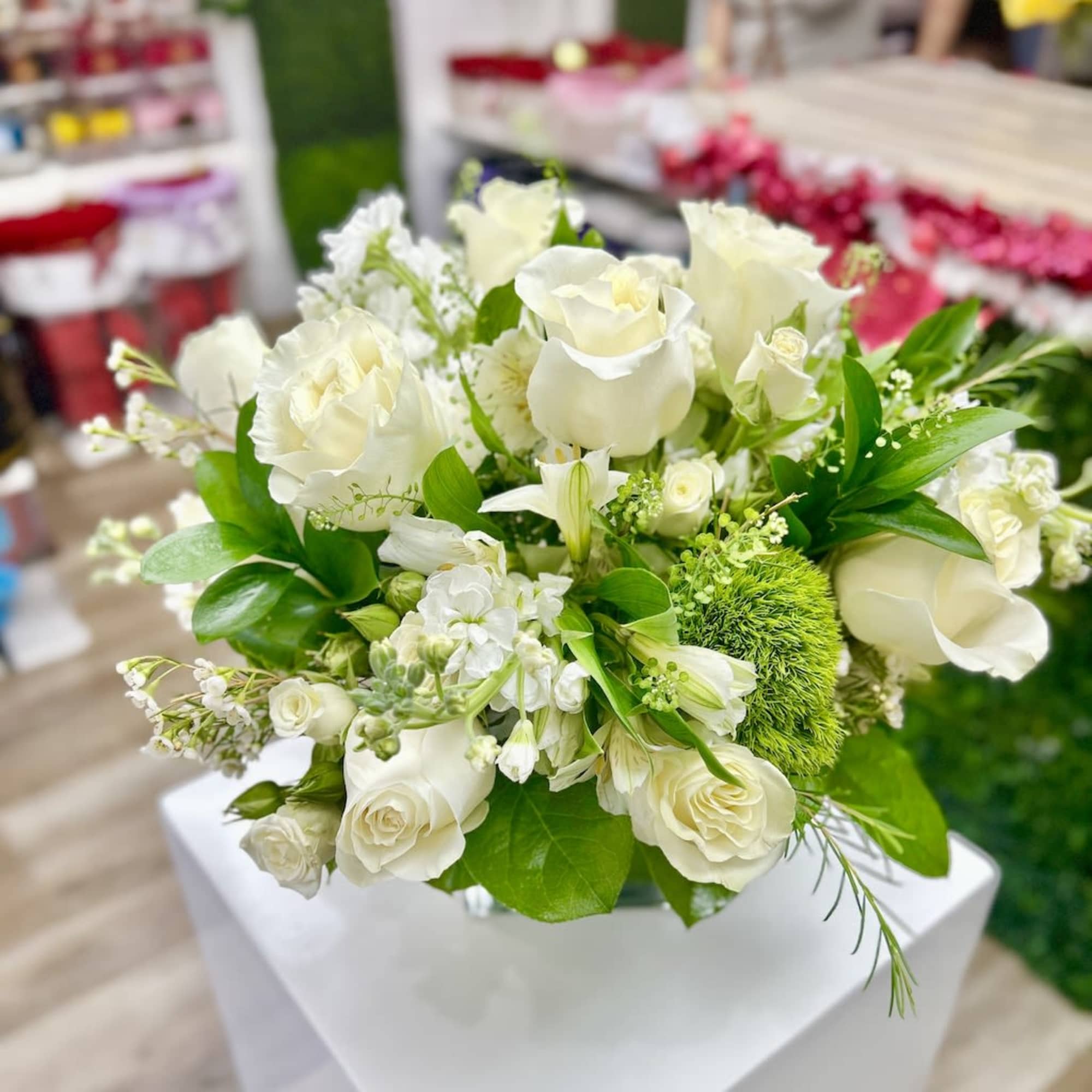 Arrangement of white roses and mixed white flowers with green accents in a clear glass vase