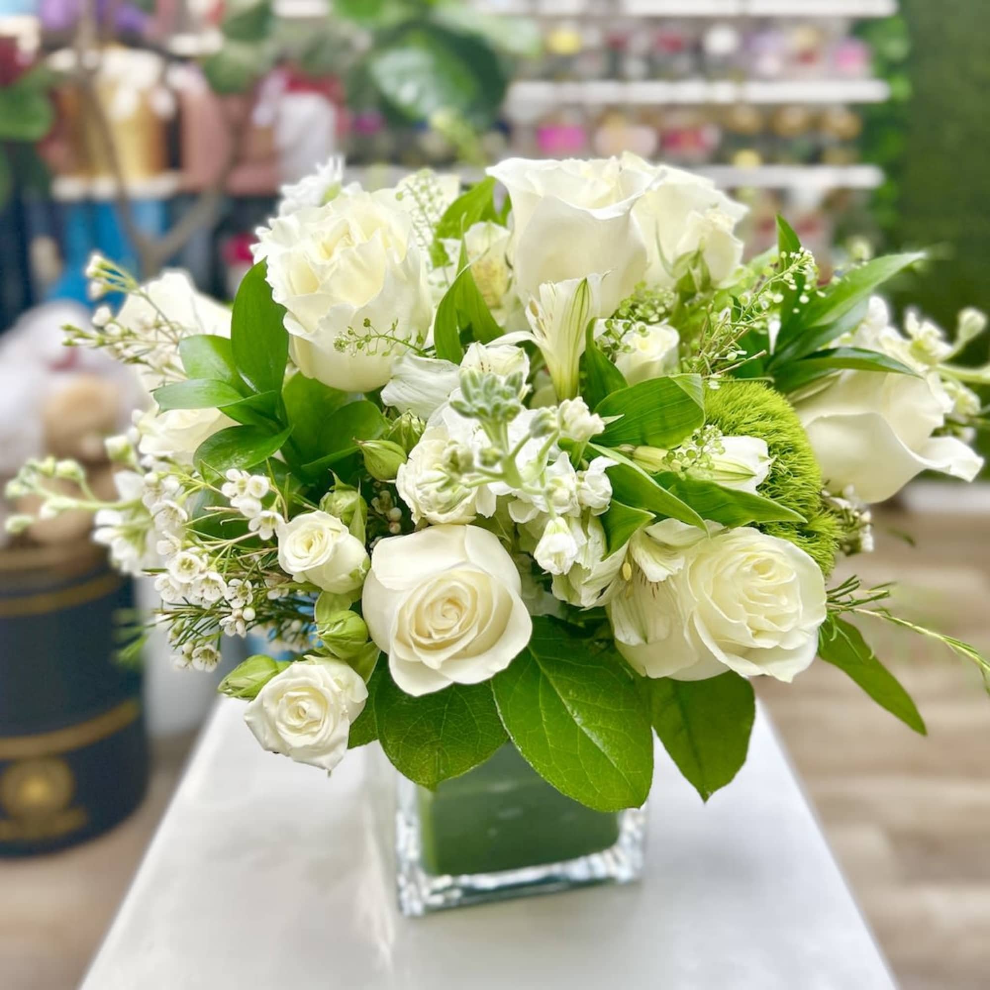 Compact white rose and mixed flower arrangement in a clear glass cube vase