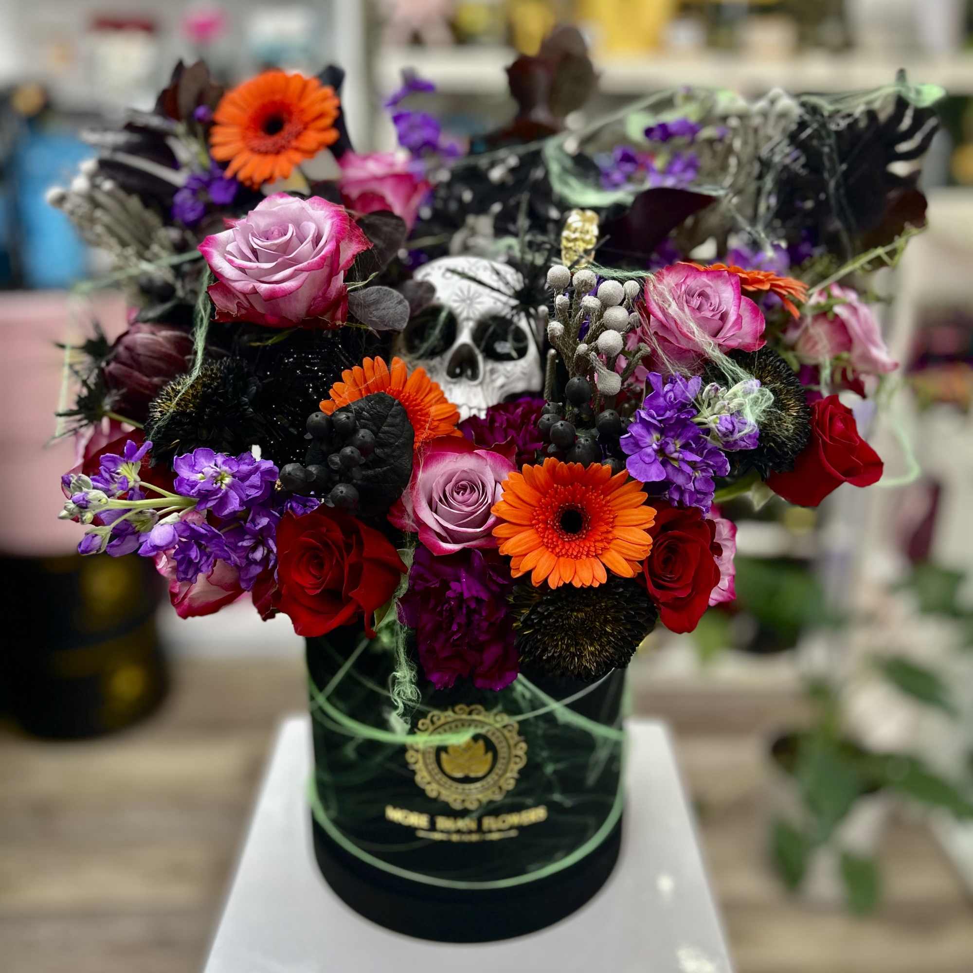 Halloween flower hatbox with bright roses, gerberas, purple blooms and a skull decoration.