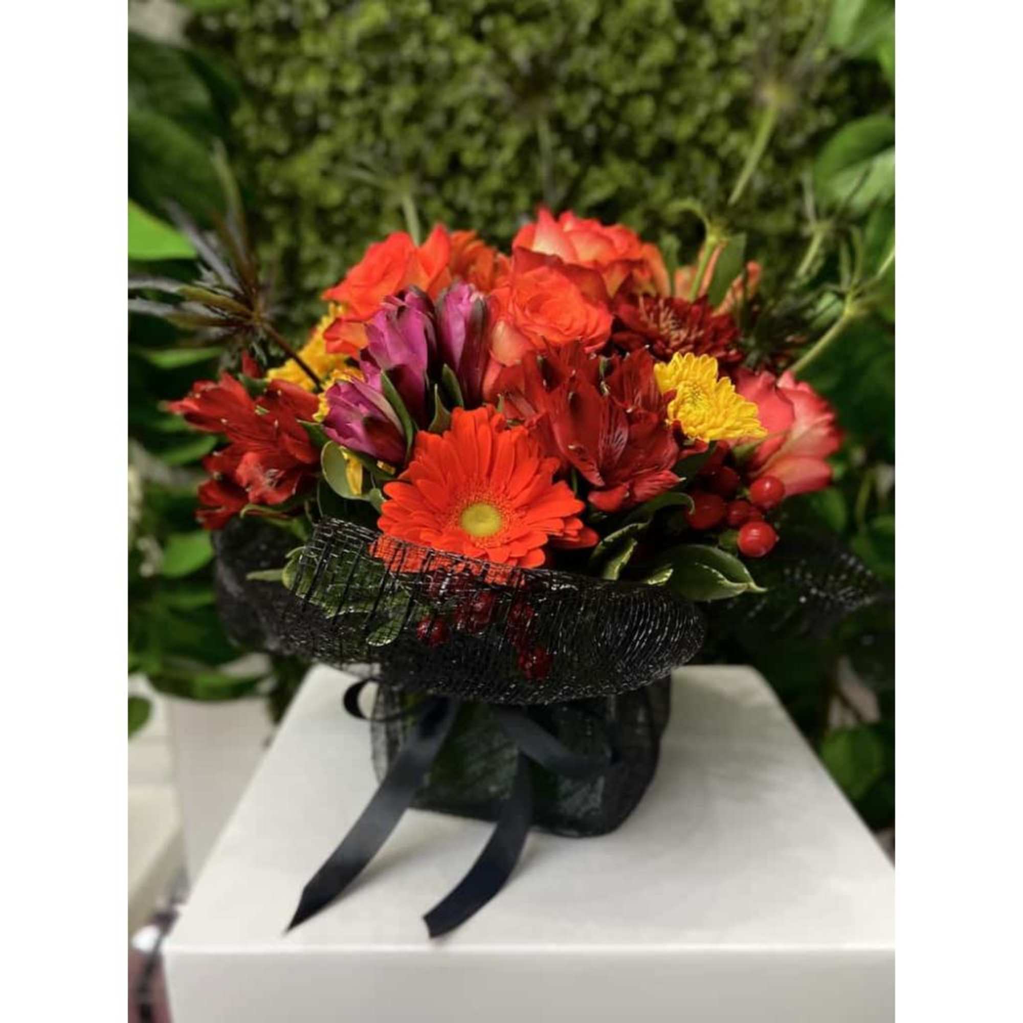 Bright bouquet of red and orange flowers with yellow accents wrapped in black mesh with a ribbon.