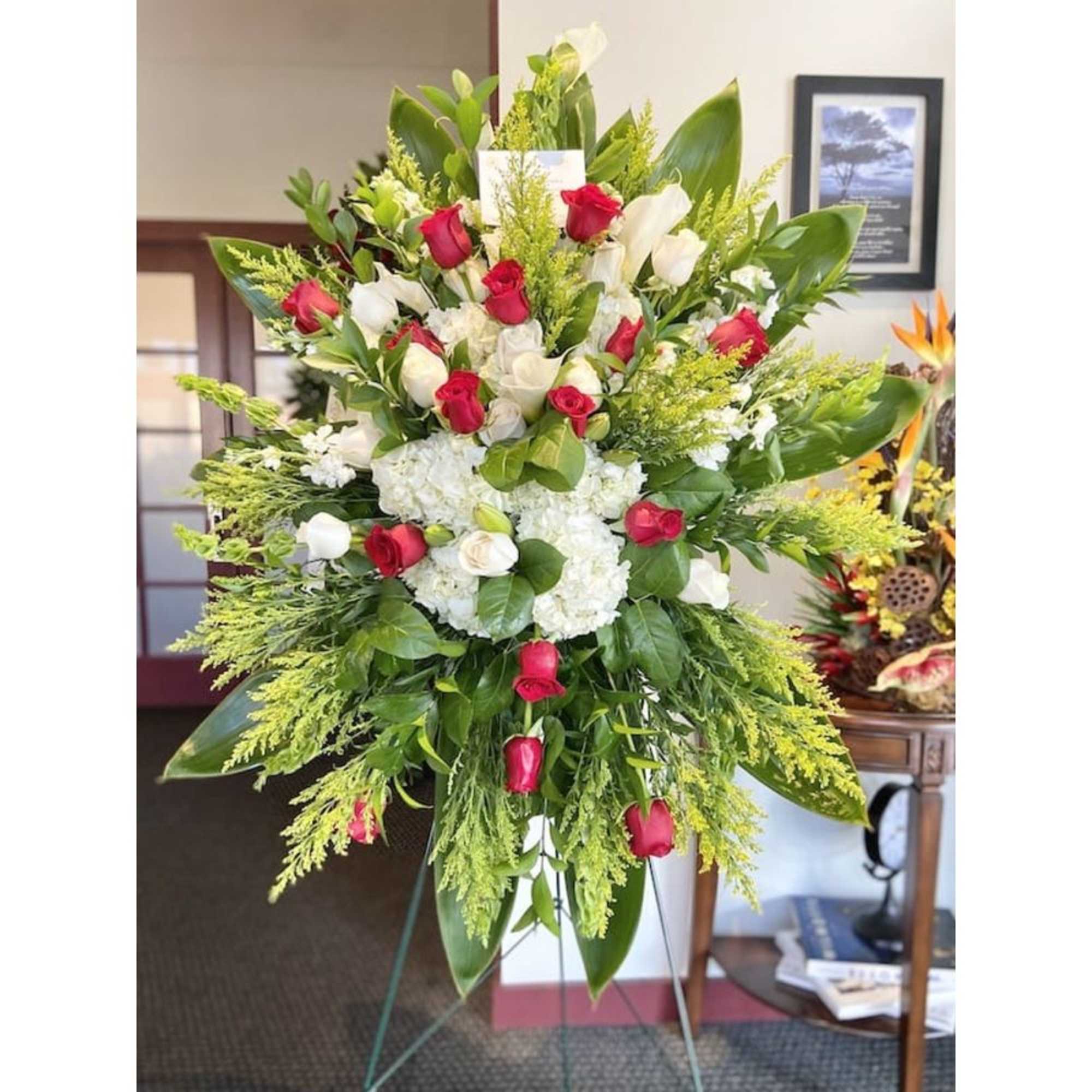 Tall standing spray of red and white roses with white hydrangeas on an easel.