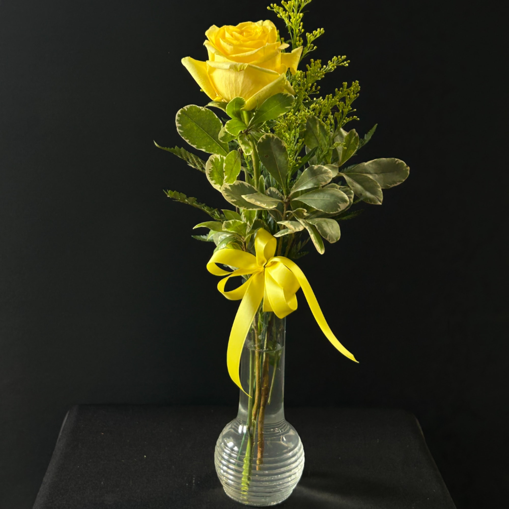 Yellow rose in a clear glass vase with a yellow ribbon