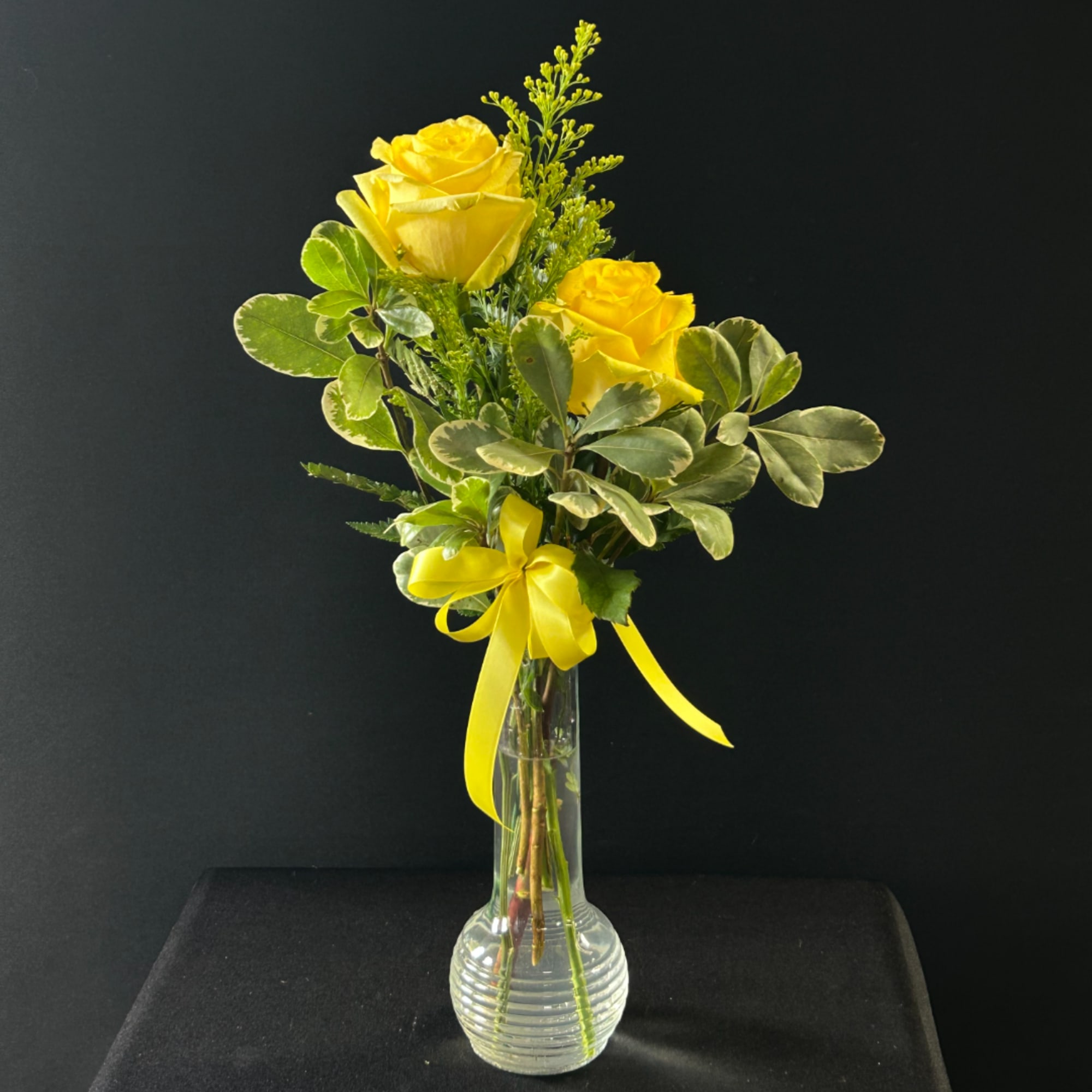 Yellow roses in a clear glass vase with a yellow ribbon