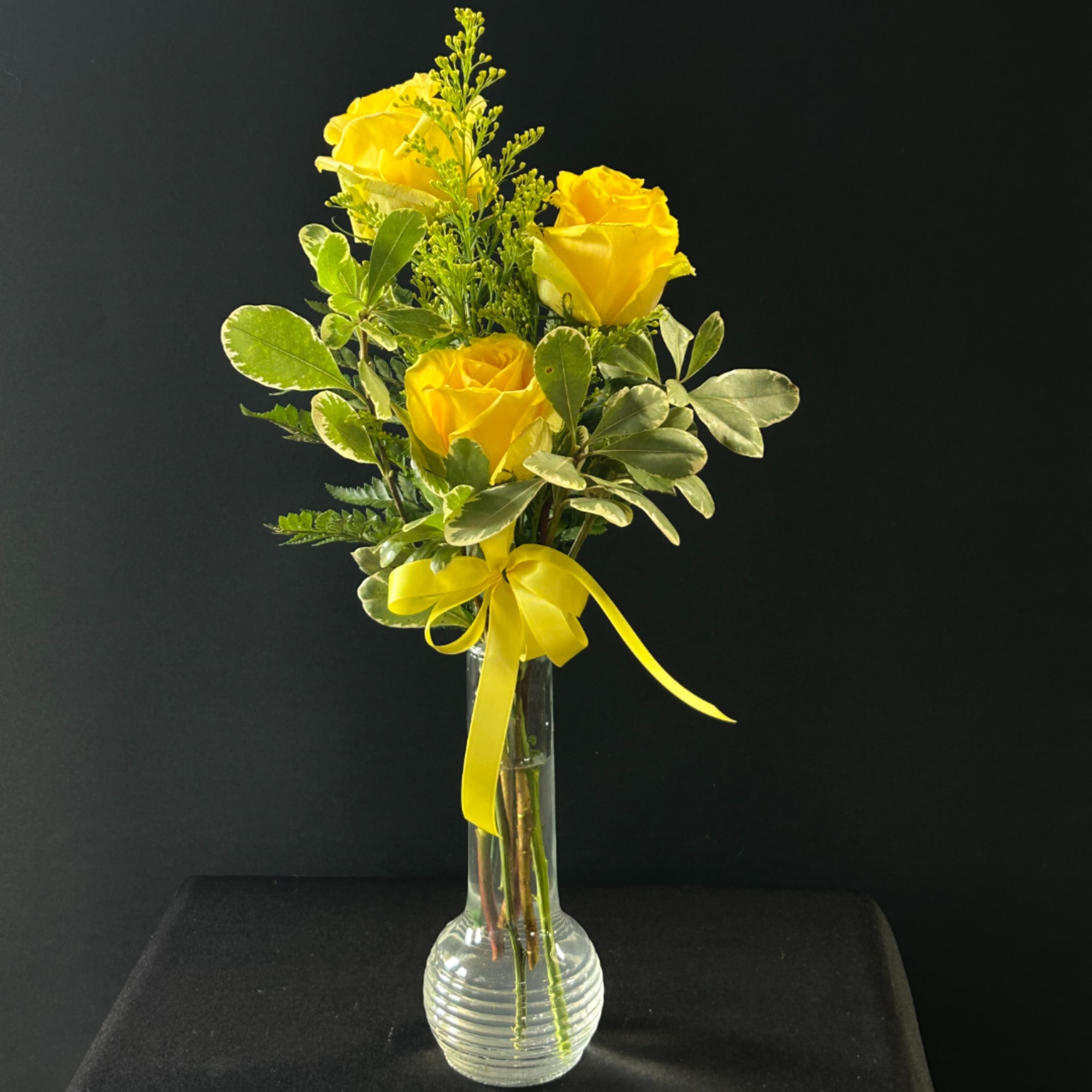 Yellow roses in a clear glass vase with a yellow ribbon