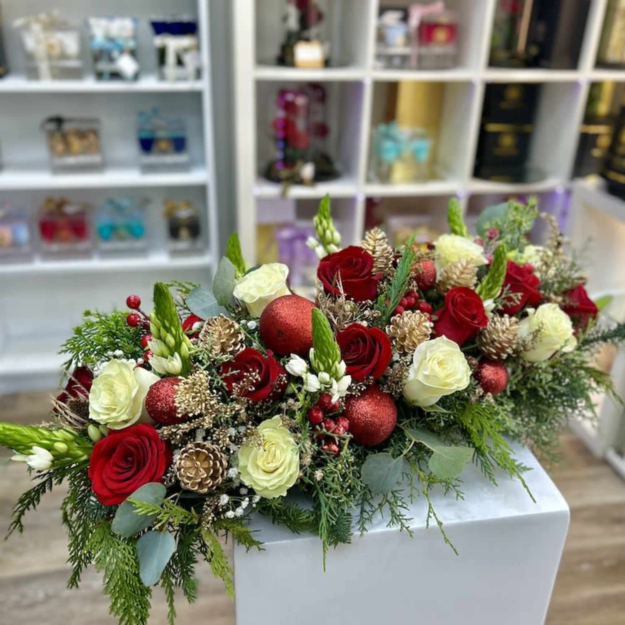 Long low arrangement of red and cream roses with evergreens, gold pinecones, and red ornaments.
