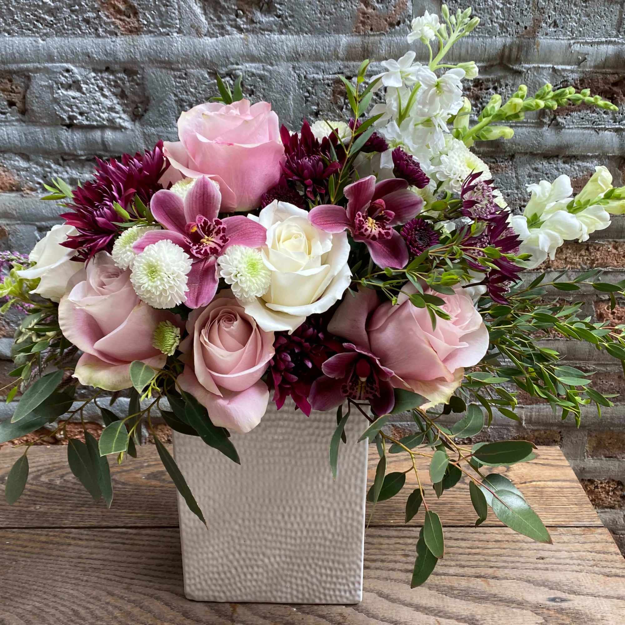 Pink and white roses with purple orchids in a white vase
