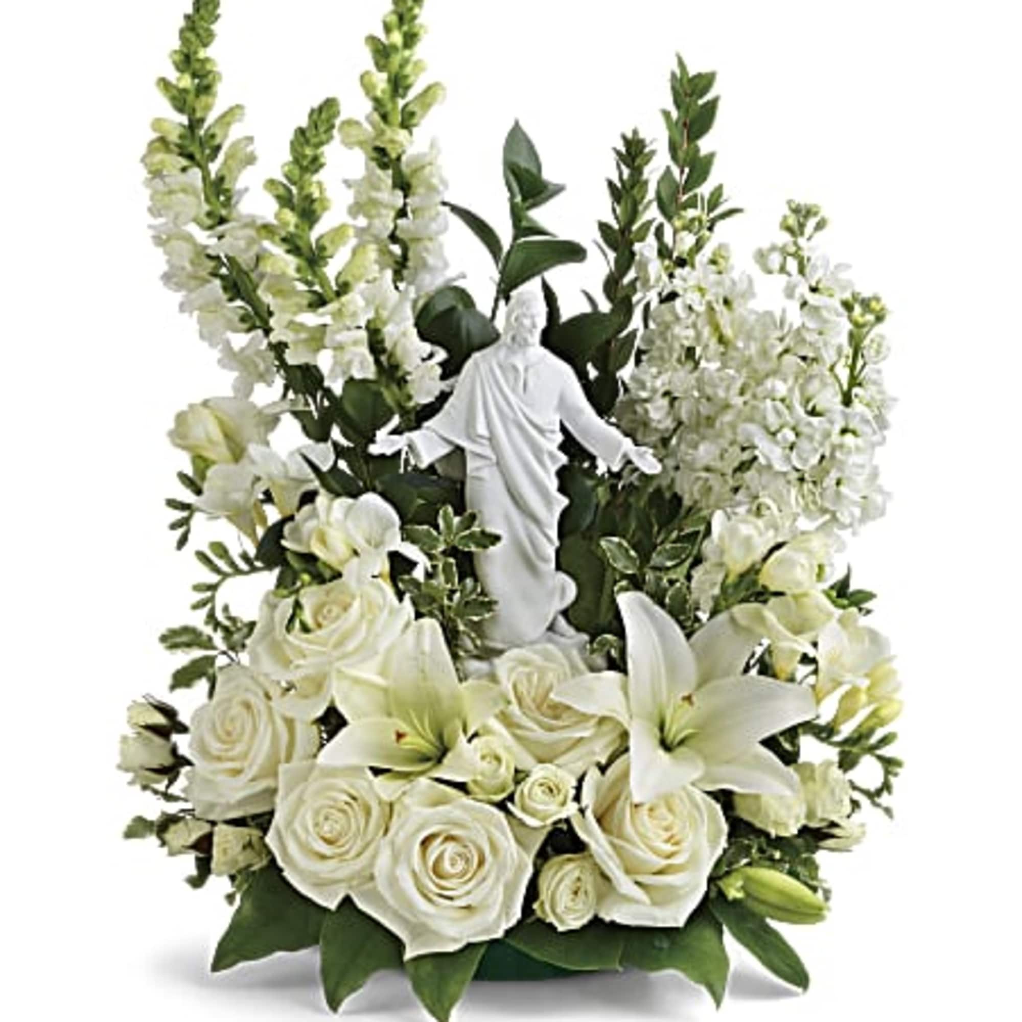White roses and lilies arranged around a small white religious statue