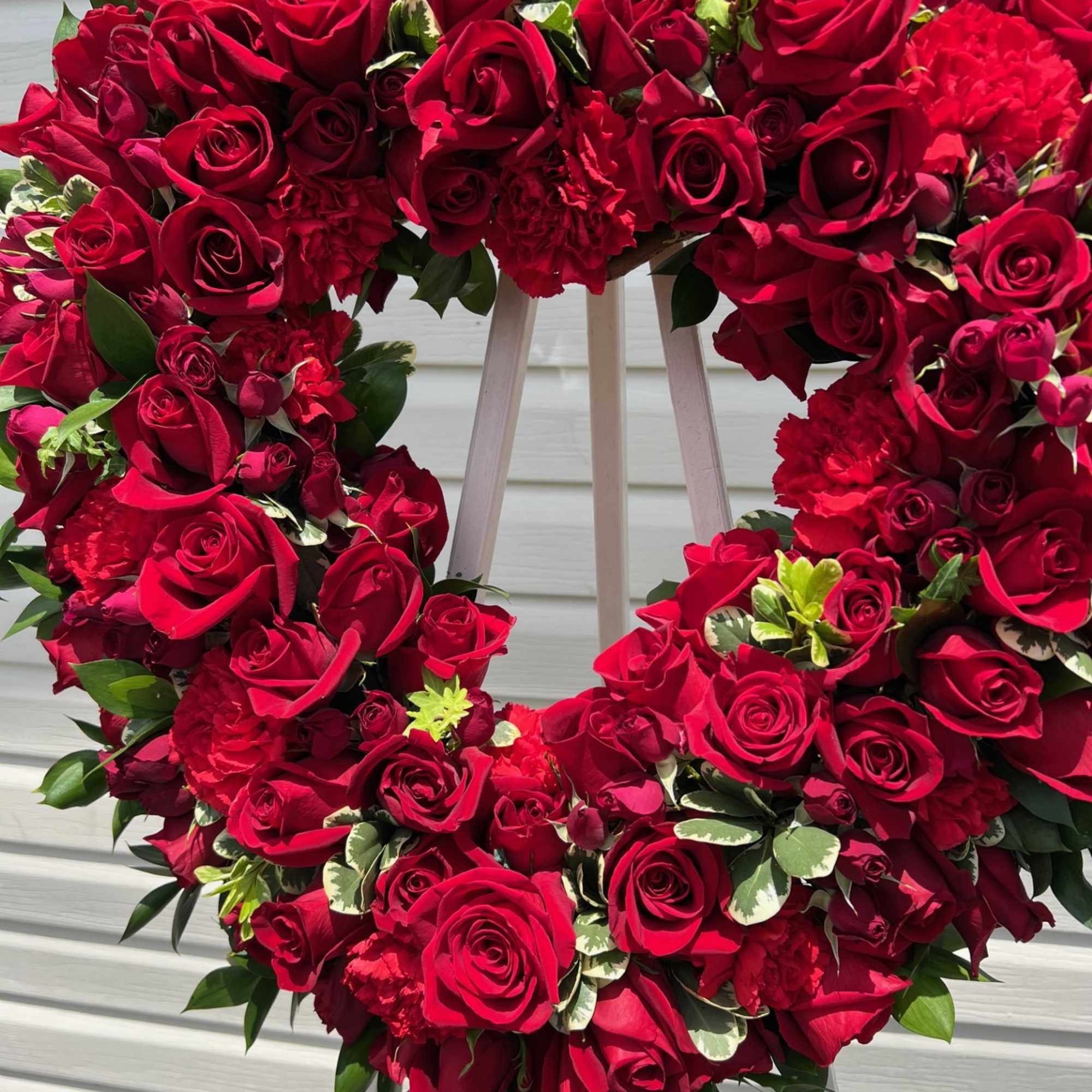 Heart-shaped wreath of red roses and carnations on an easel
