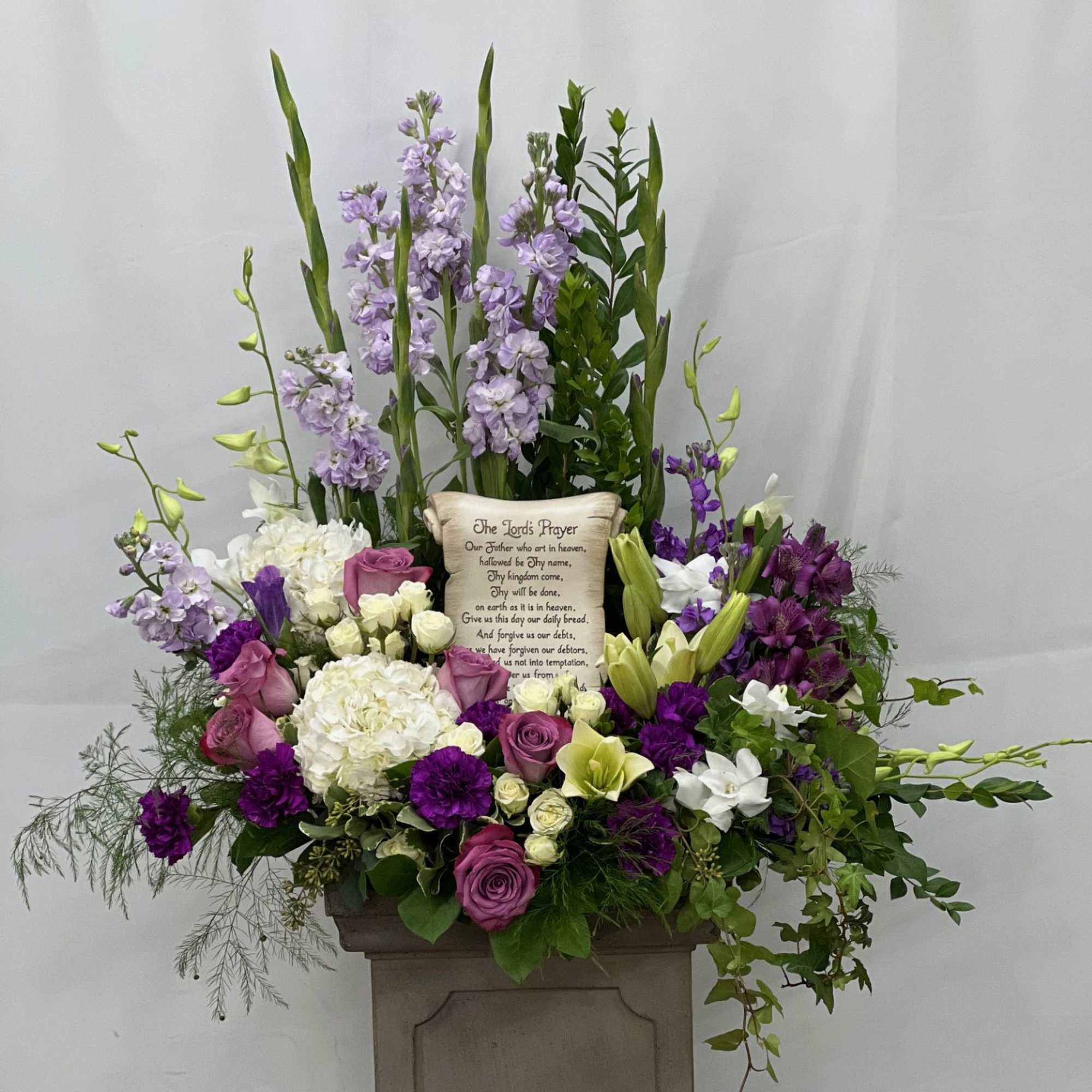 Large floral arrangement with purple, white, and green flowers around a prayer plaque