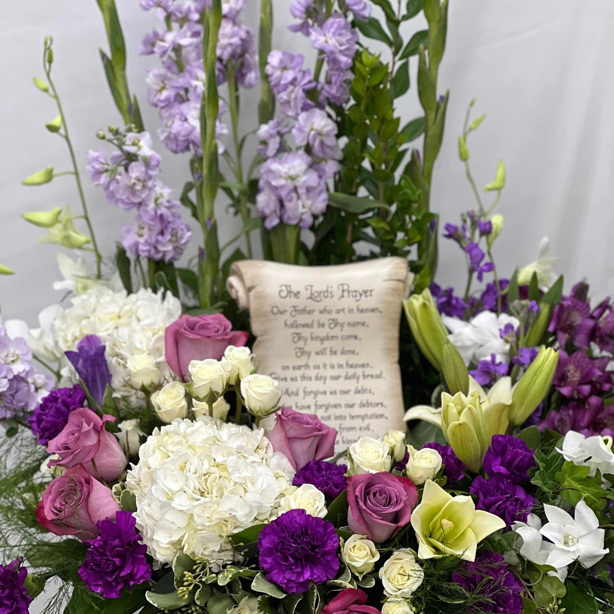 Purple and white floral arrangement with a prayer scroll centerpiece