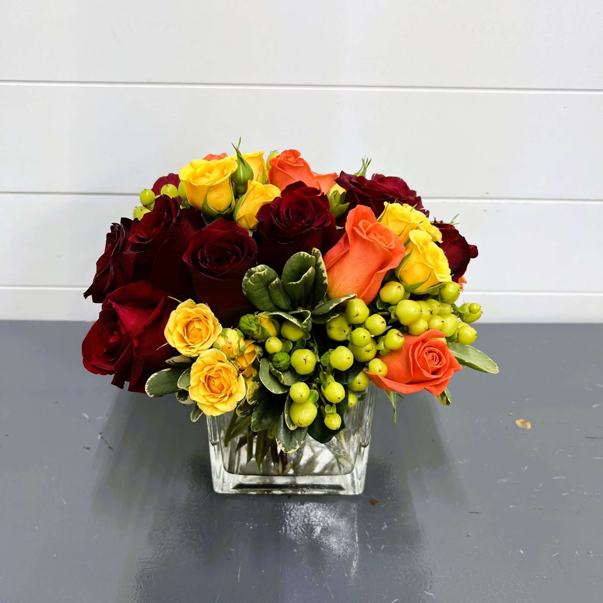 Bouquet of red, orange, and yellow roses in a clear glass vase