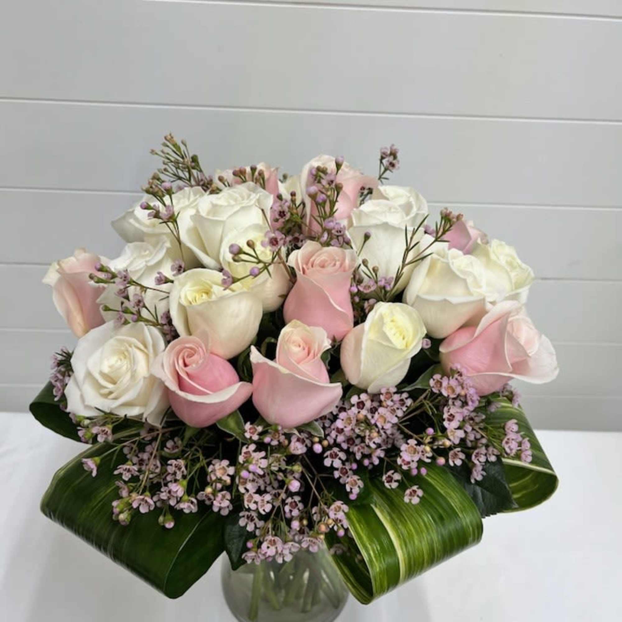 Round arrangement of white and pale pink roses with tiny pink filler flowers in a clear glass vase