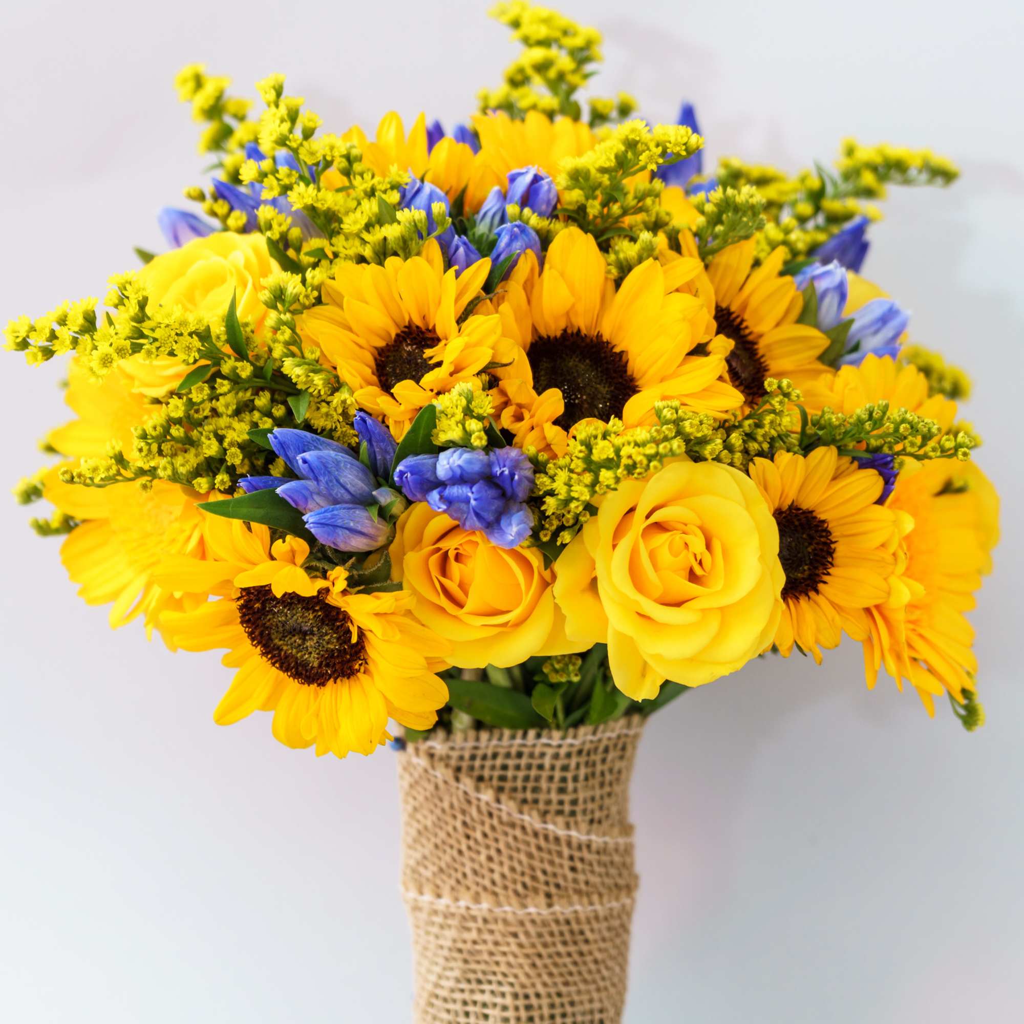 Bouquet of yellow sunflowers and roses with blue flowers wrapped in burlap