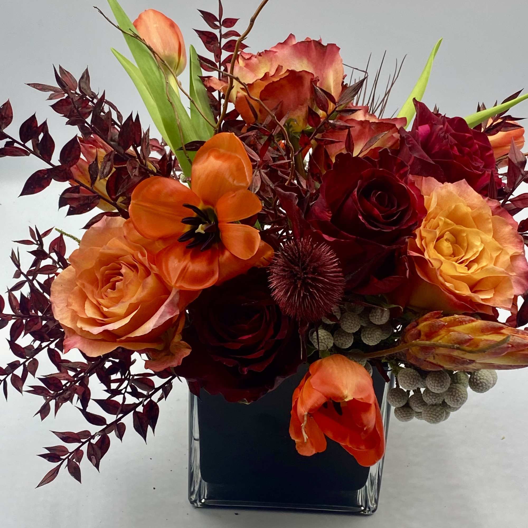 Orange and red roses with tulips in a square glass vase