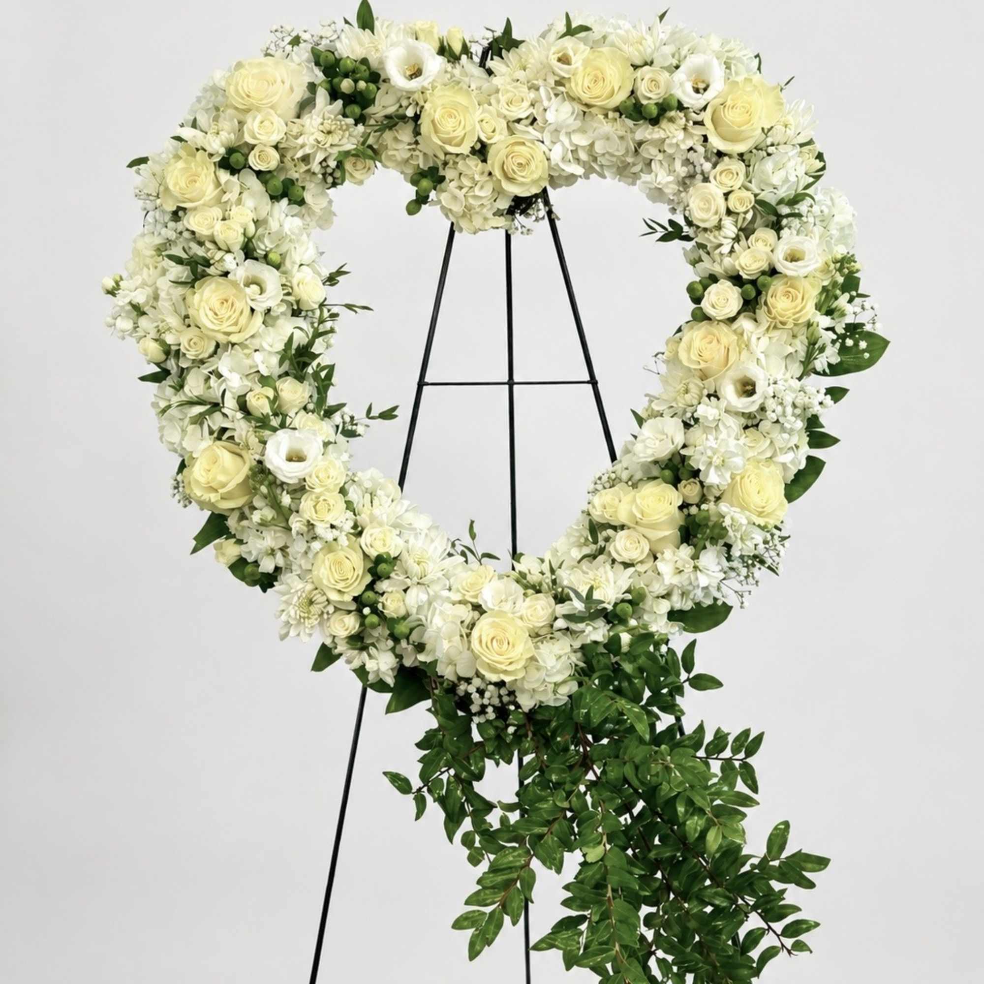 Heart-shaped floral wreath of white and pale yellow flowers on a black stand