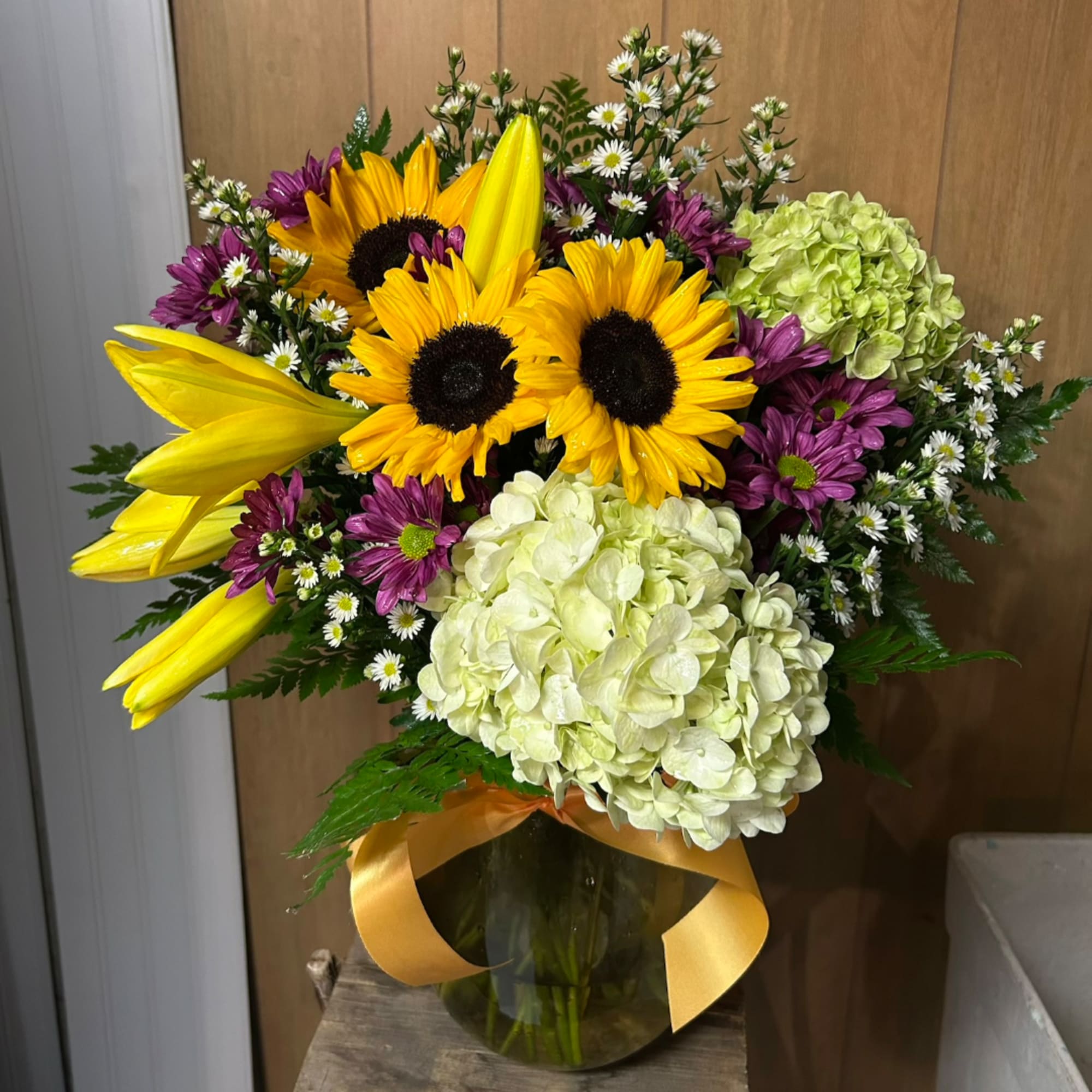 Bouquet of sunflowers, lilies, hydrangeas, and purple daisies in a glass vase