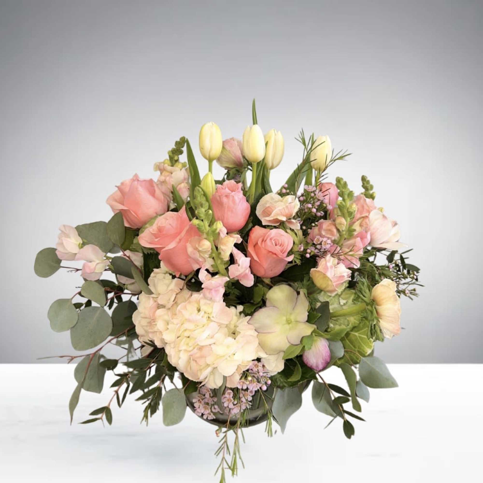A romantic floral centerpiece featuring blush roses, lilies, tulips, and fresh greenery