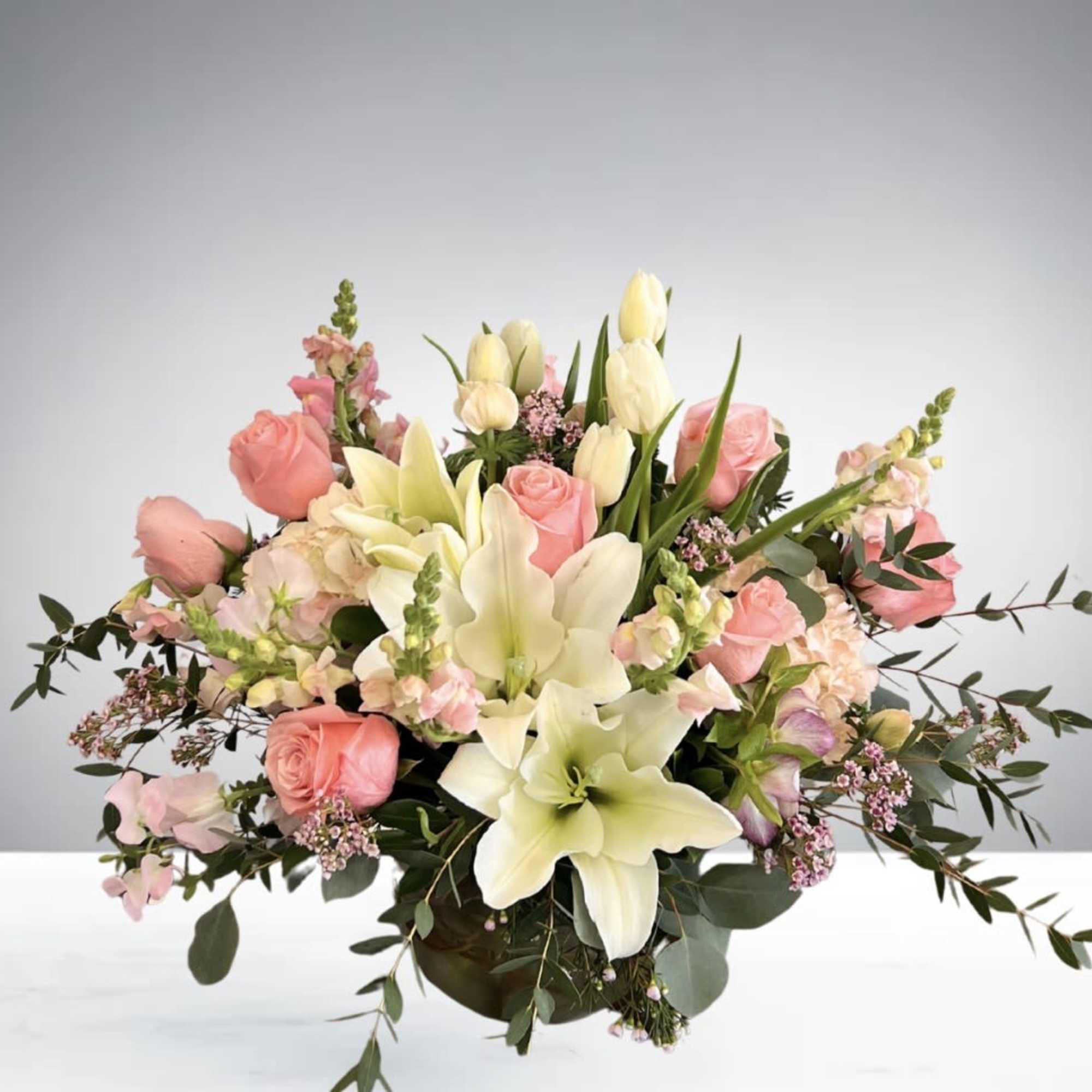 A romantic floral centerpiece featuring blush roses, lilies, tulips, and fresh greenery