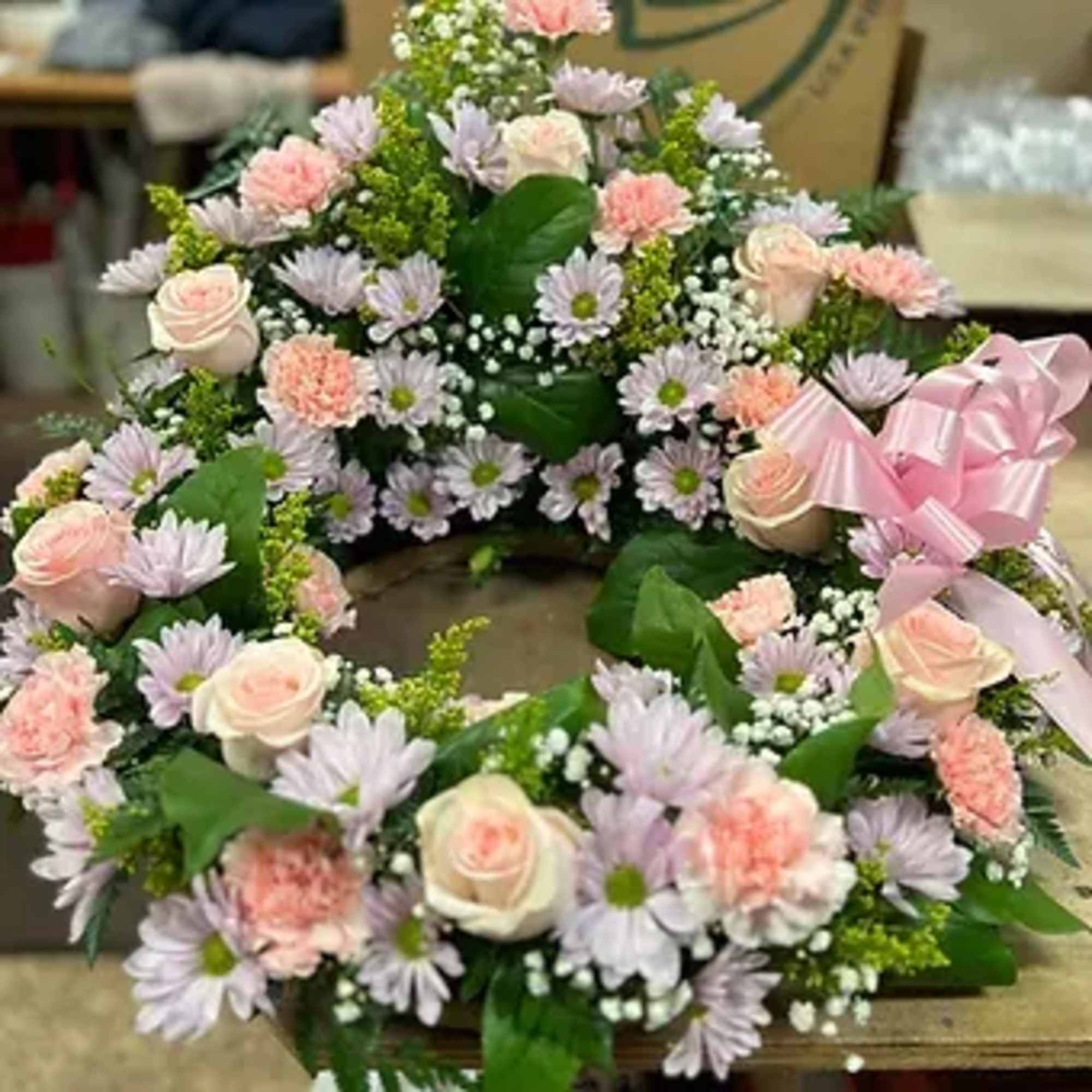 Pastel floral wreath with roses, daisies, and carnations tied with a pink ribbon
