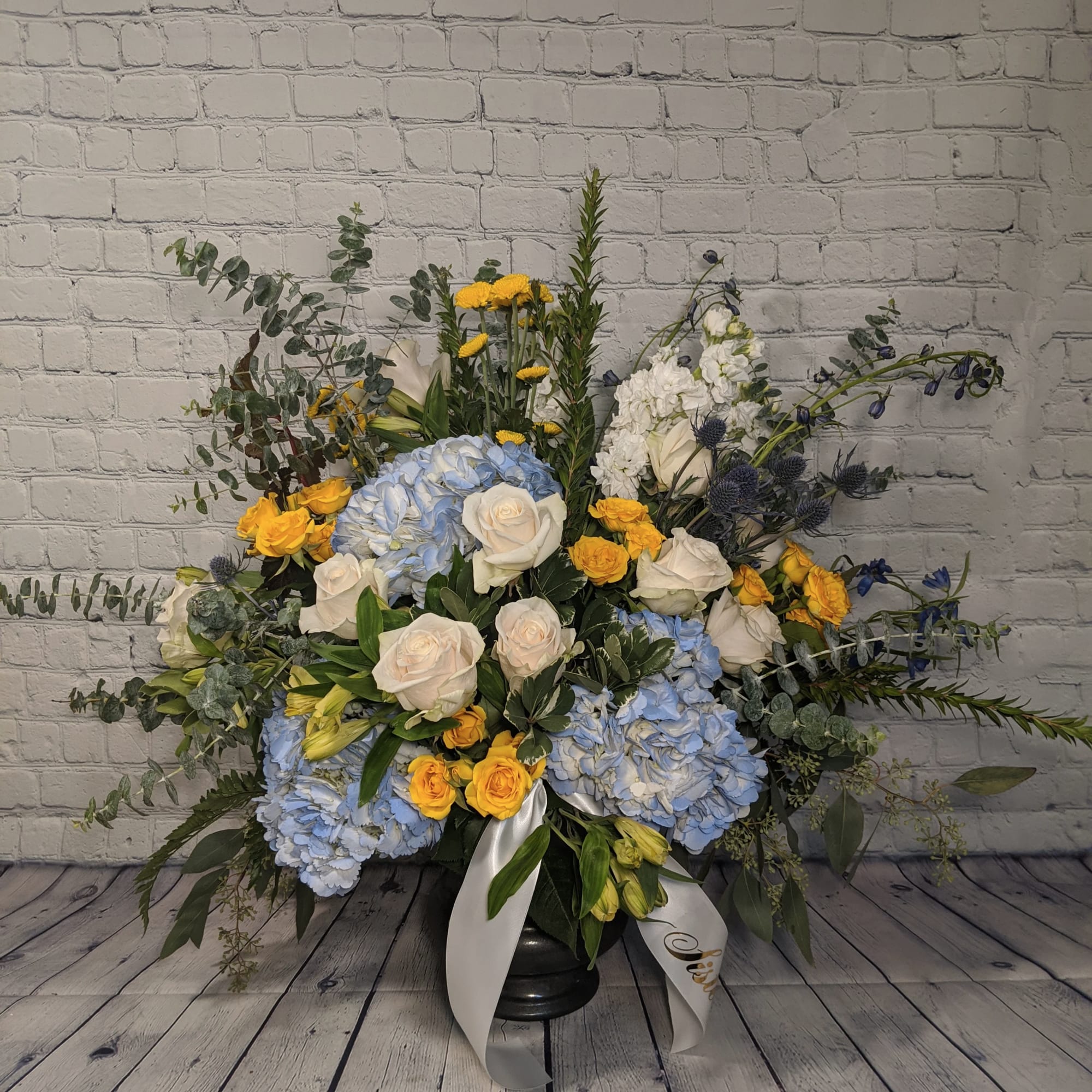 Large floral arrangement with blue hydrangeas, white roses, and yellow roses in a black vase