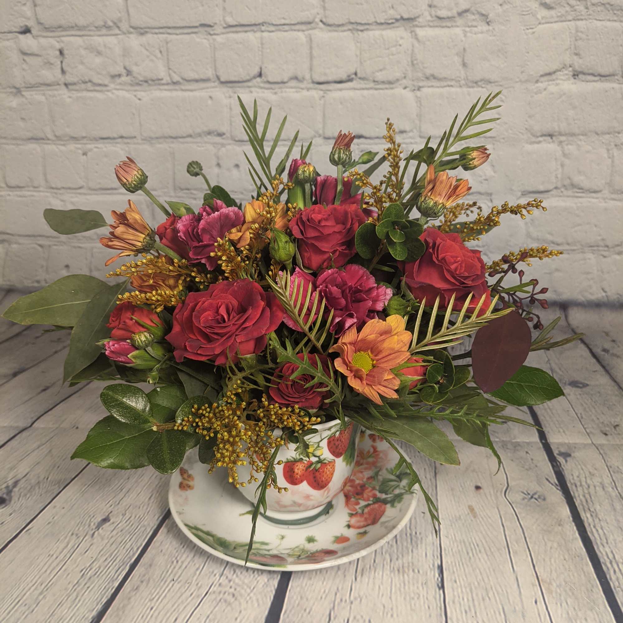 Bouquet of red roses and orange daisies in a strawberry teacup