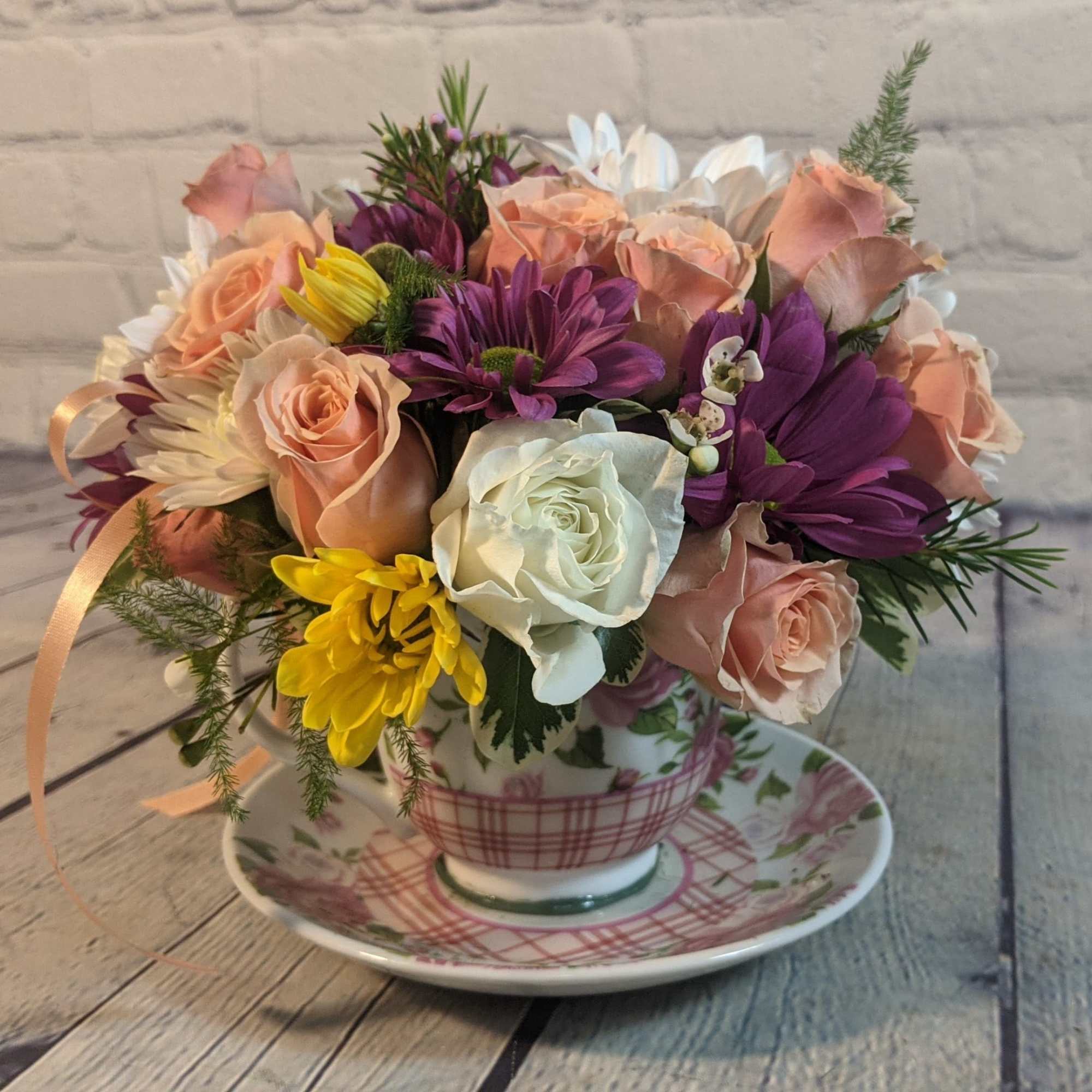 Bouquet of peach, white, purple, and yellow flowers in a teacup and saucer