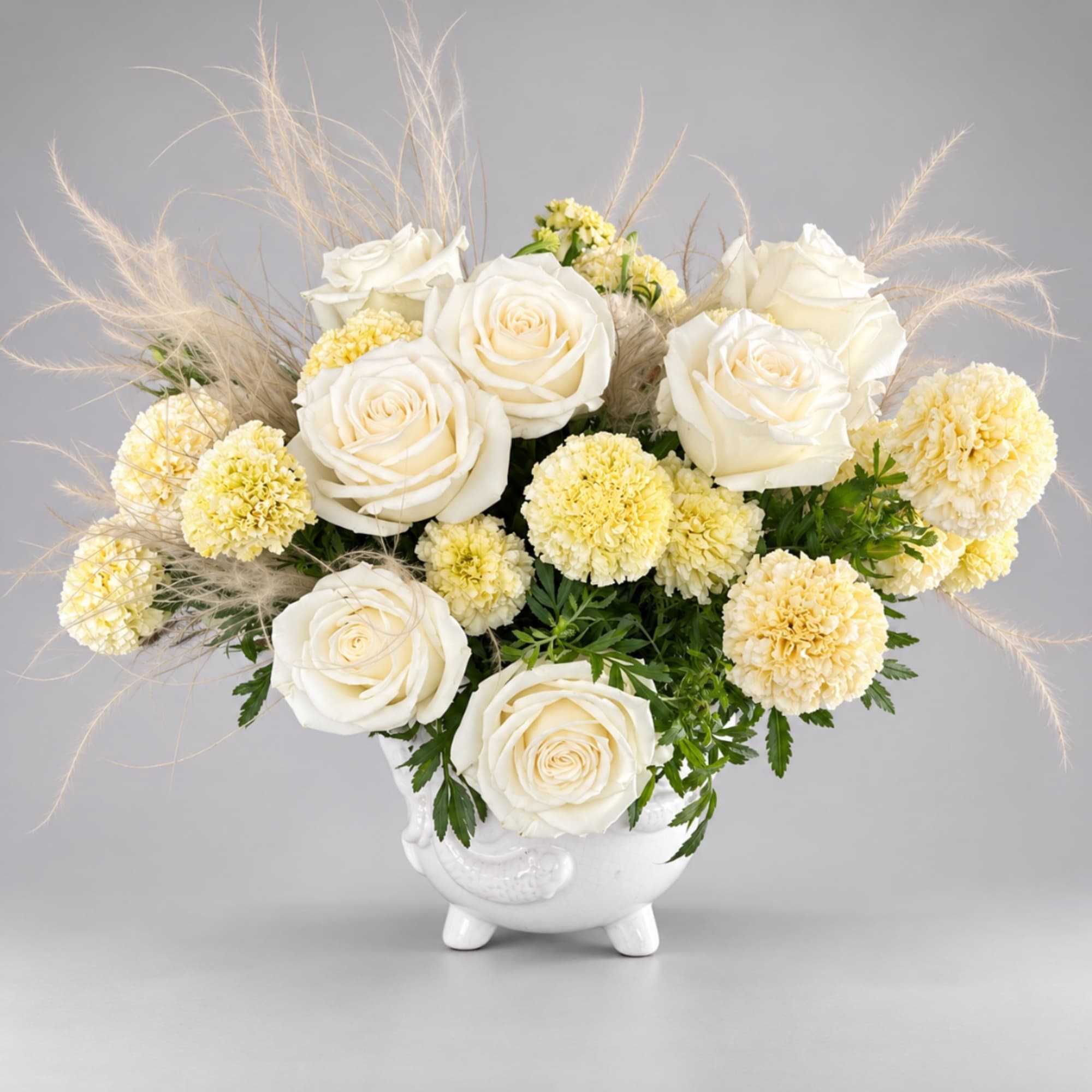 White roses and pale yellow carnations in a white vase with airy pampas grass