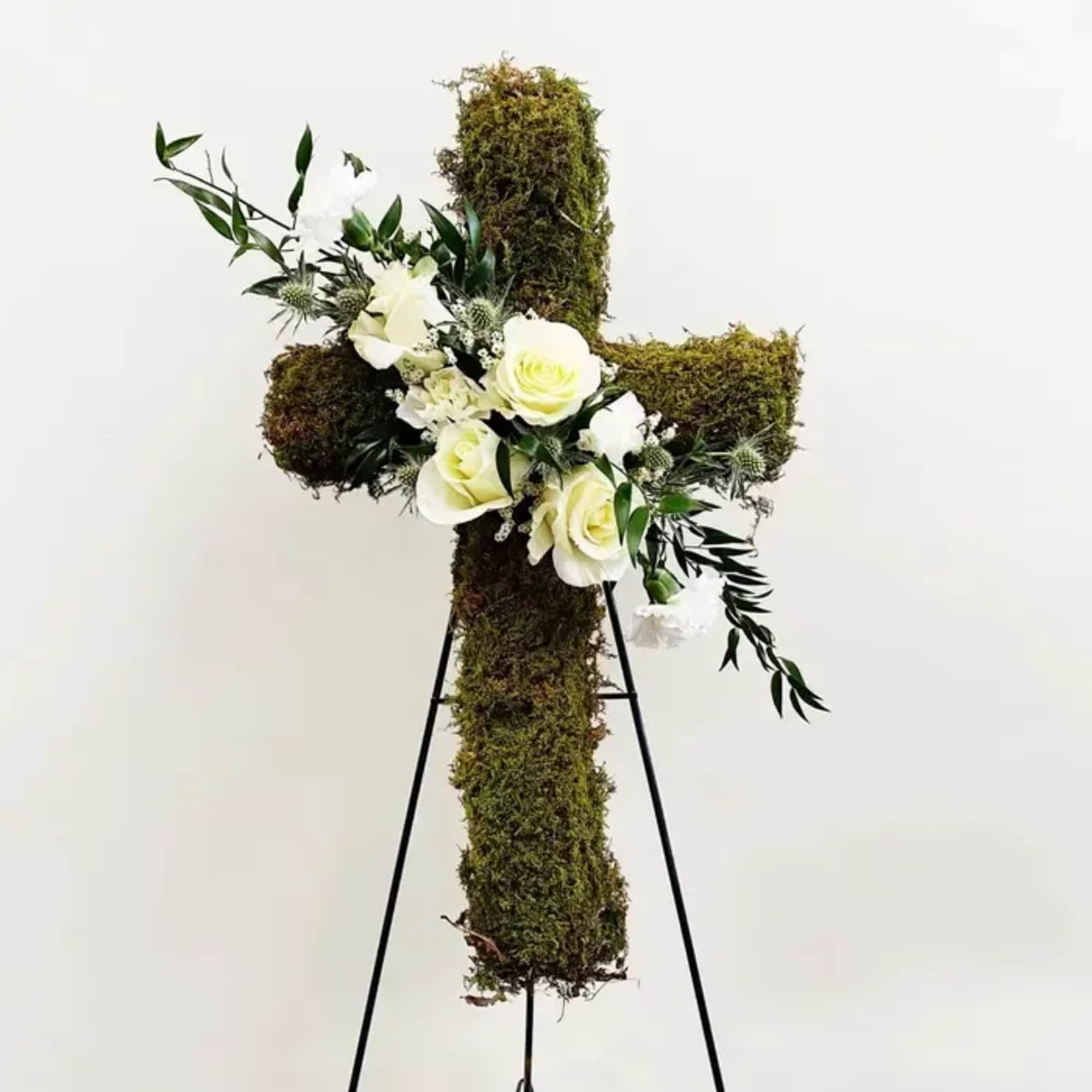 Moss-covered cross with white flowers on a stand