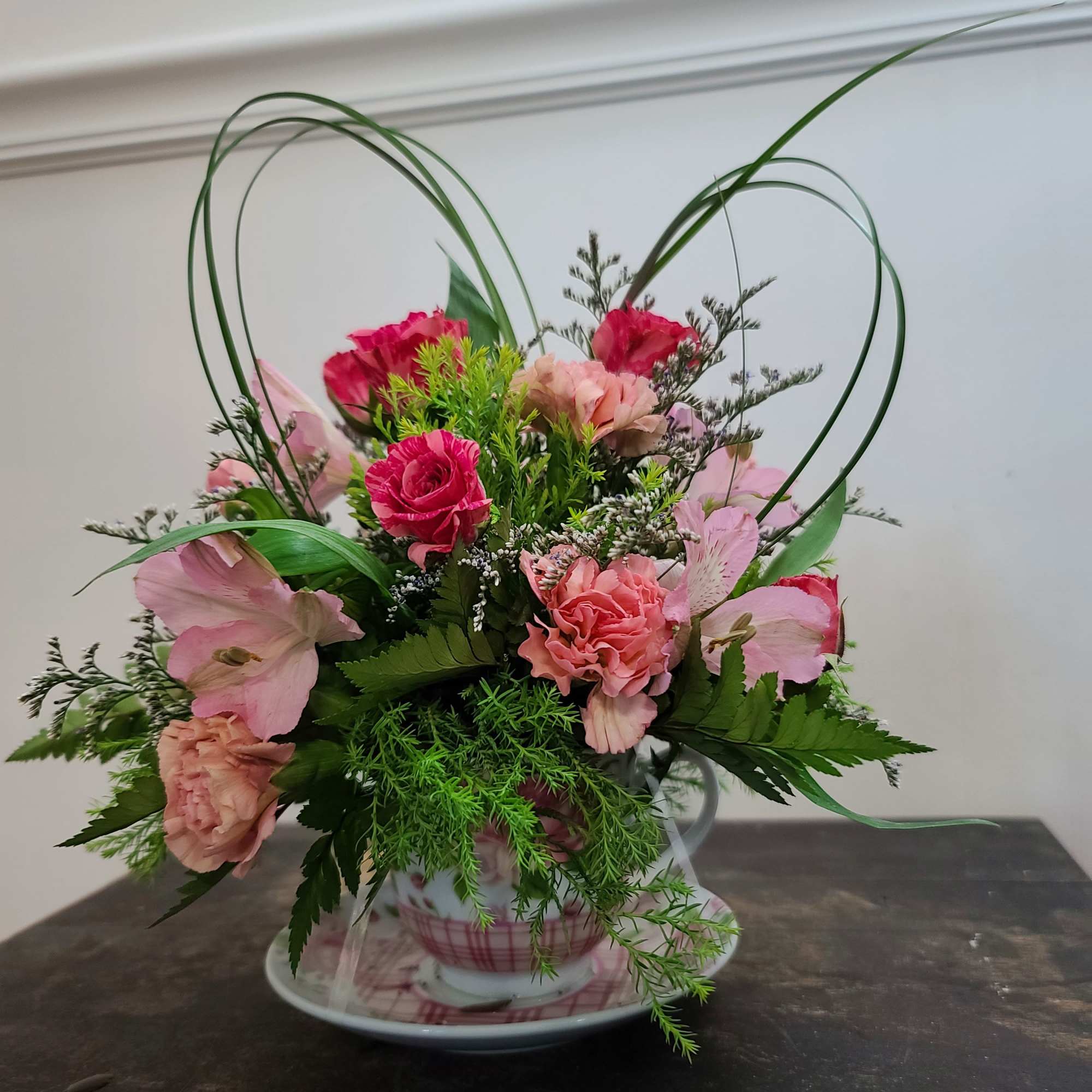 Pink floral arrangement in a teacup with heart-shaped loops