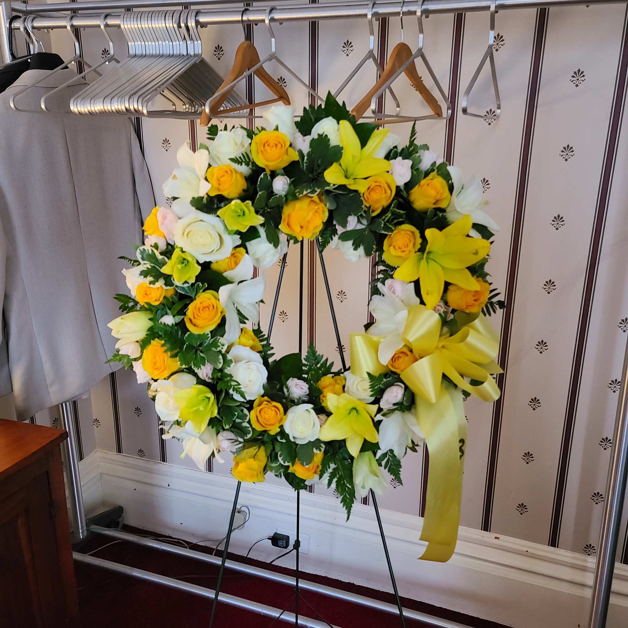 Yellow and white floral wreath on a stand with a ribbon bow