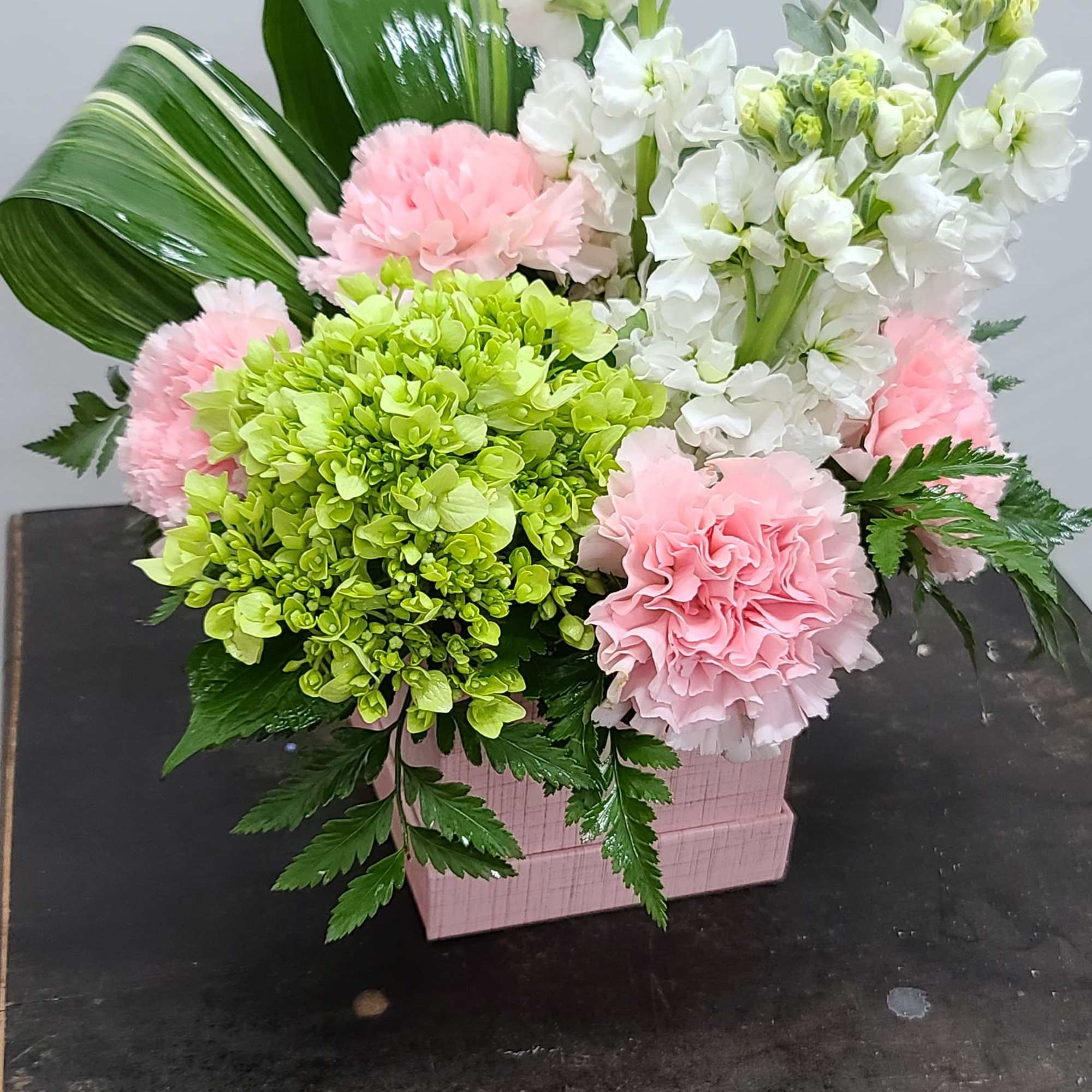 Pink and white floral arrangement in a pink box with large green leaves