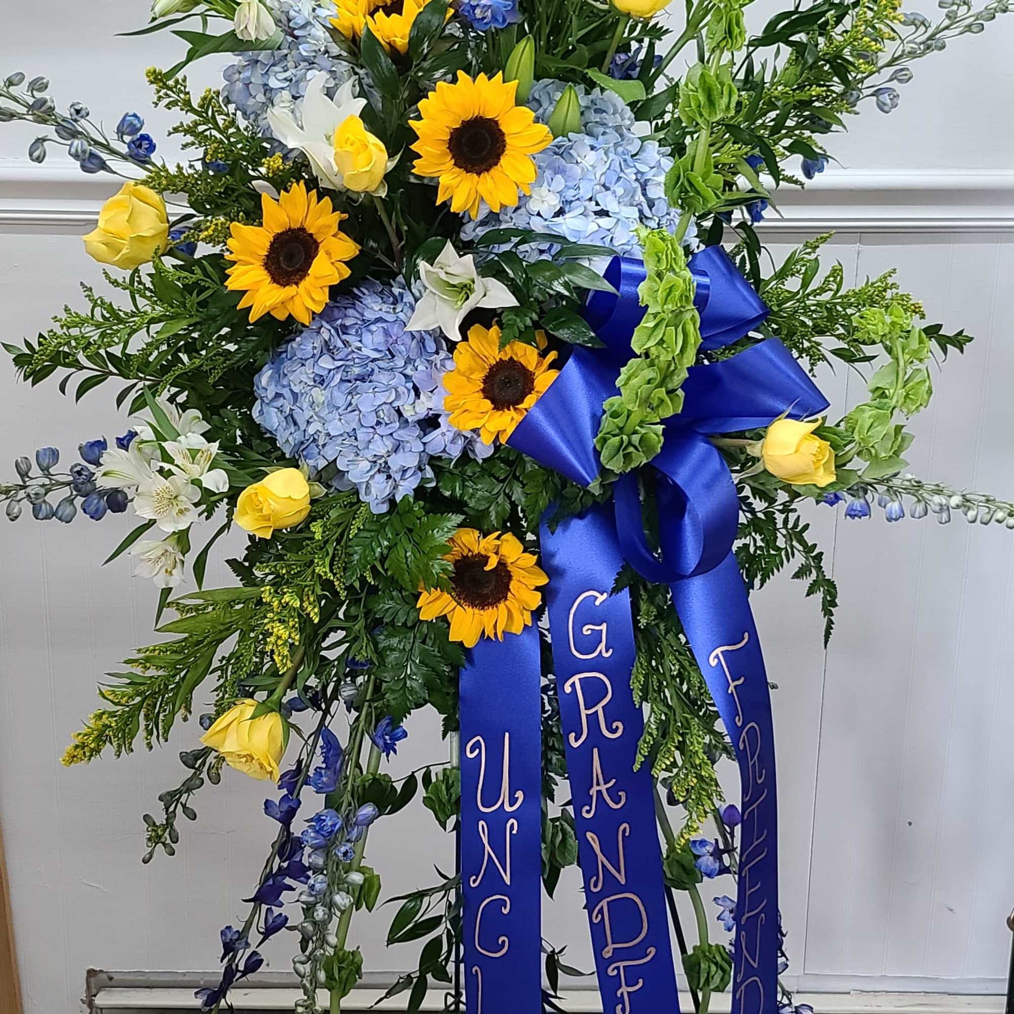Standing floral spray with sunflowers, blue hydrangeas, and yellow roses on a tripod easel