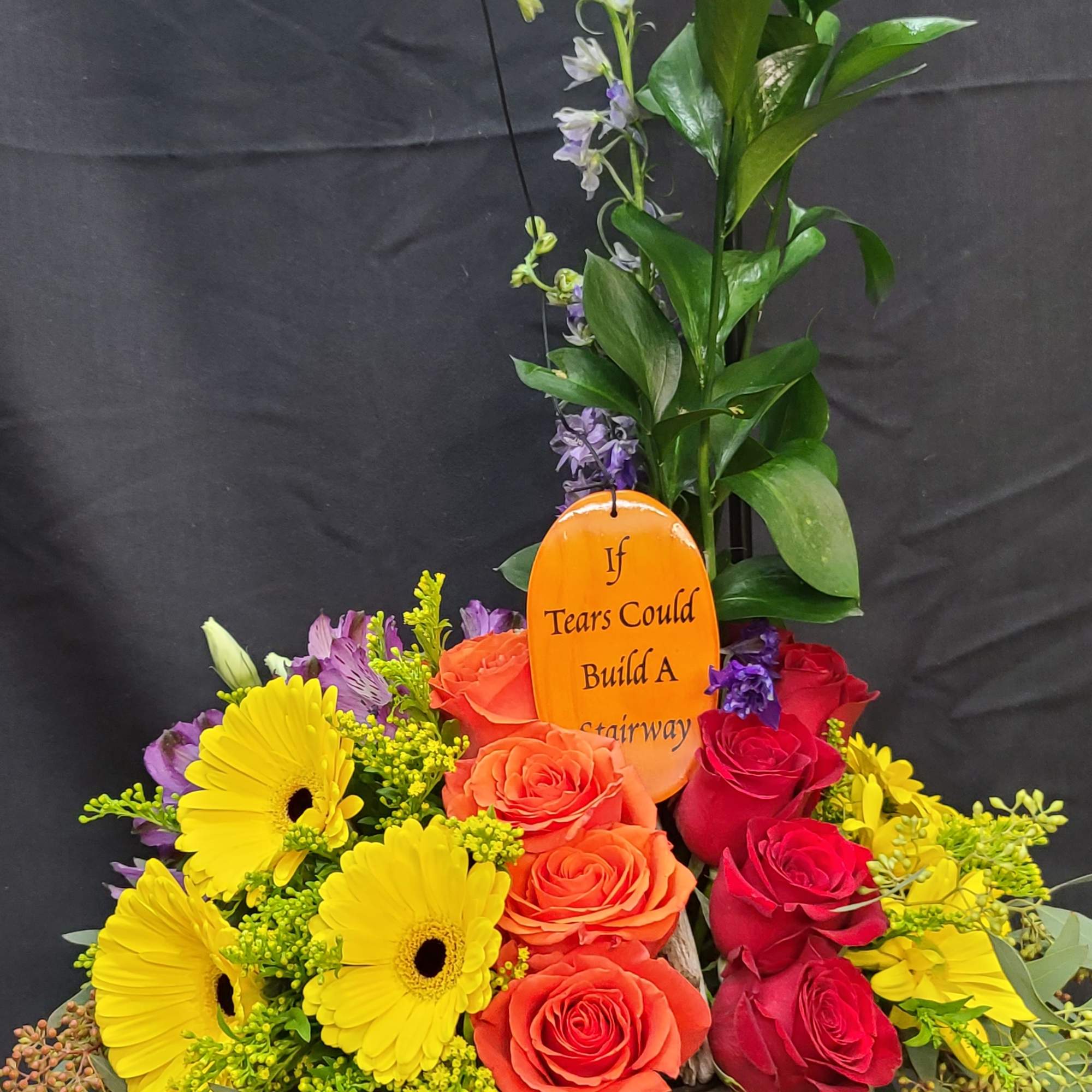 Colorful flower arrangement in a wooden bucket with a hanging memorial plaque