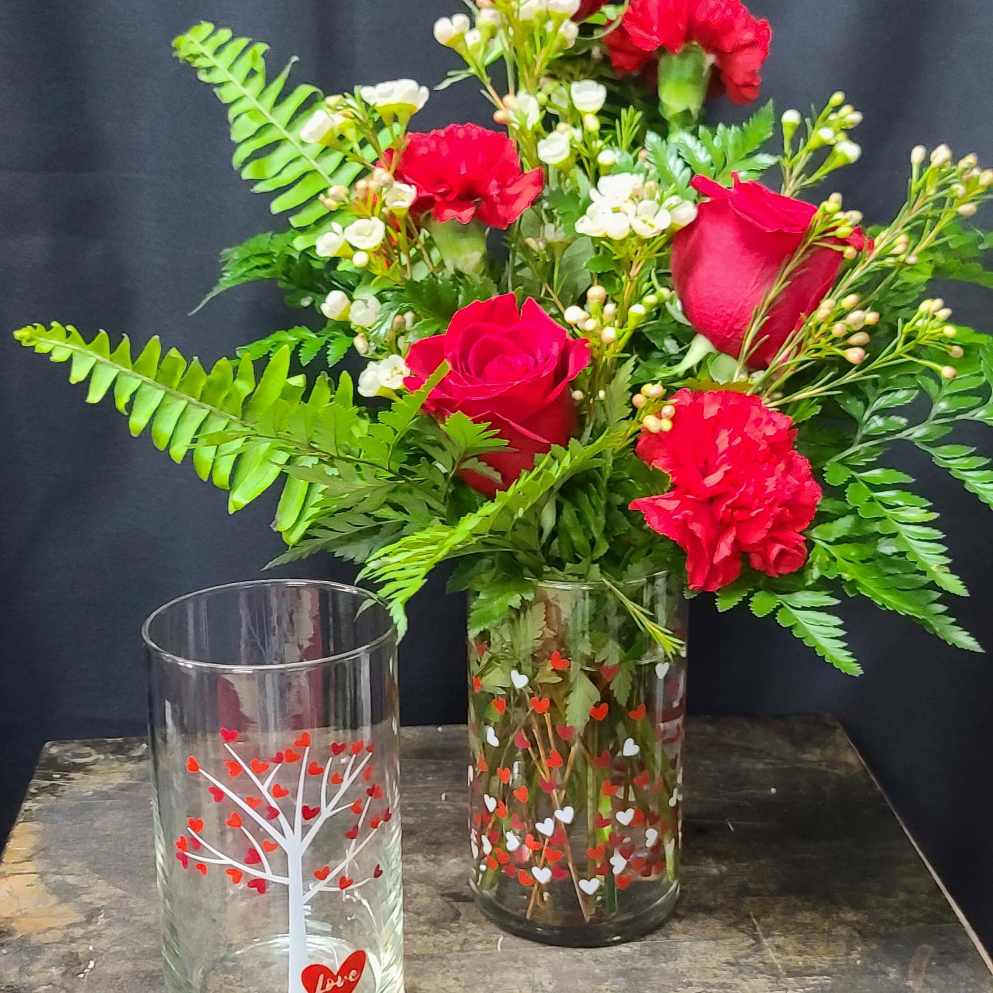 Red roses and carnations in a clear glass vase with heart decals