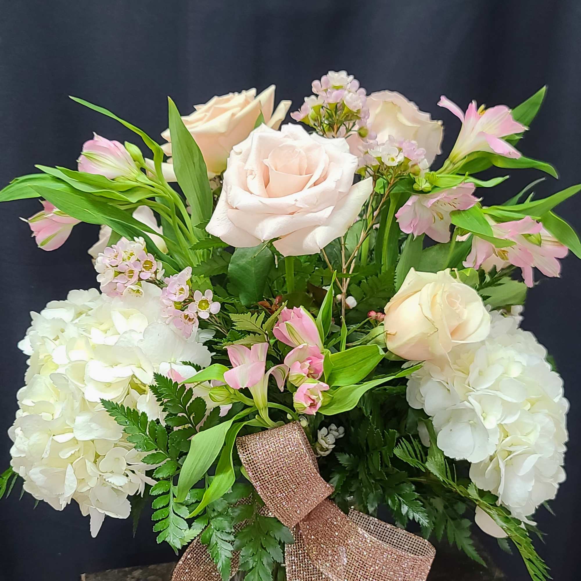 Bouquet of pale roses and white hydrangeas in a glass vase with a pink ribbon