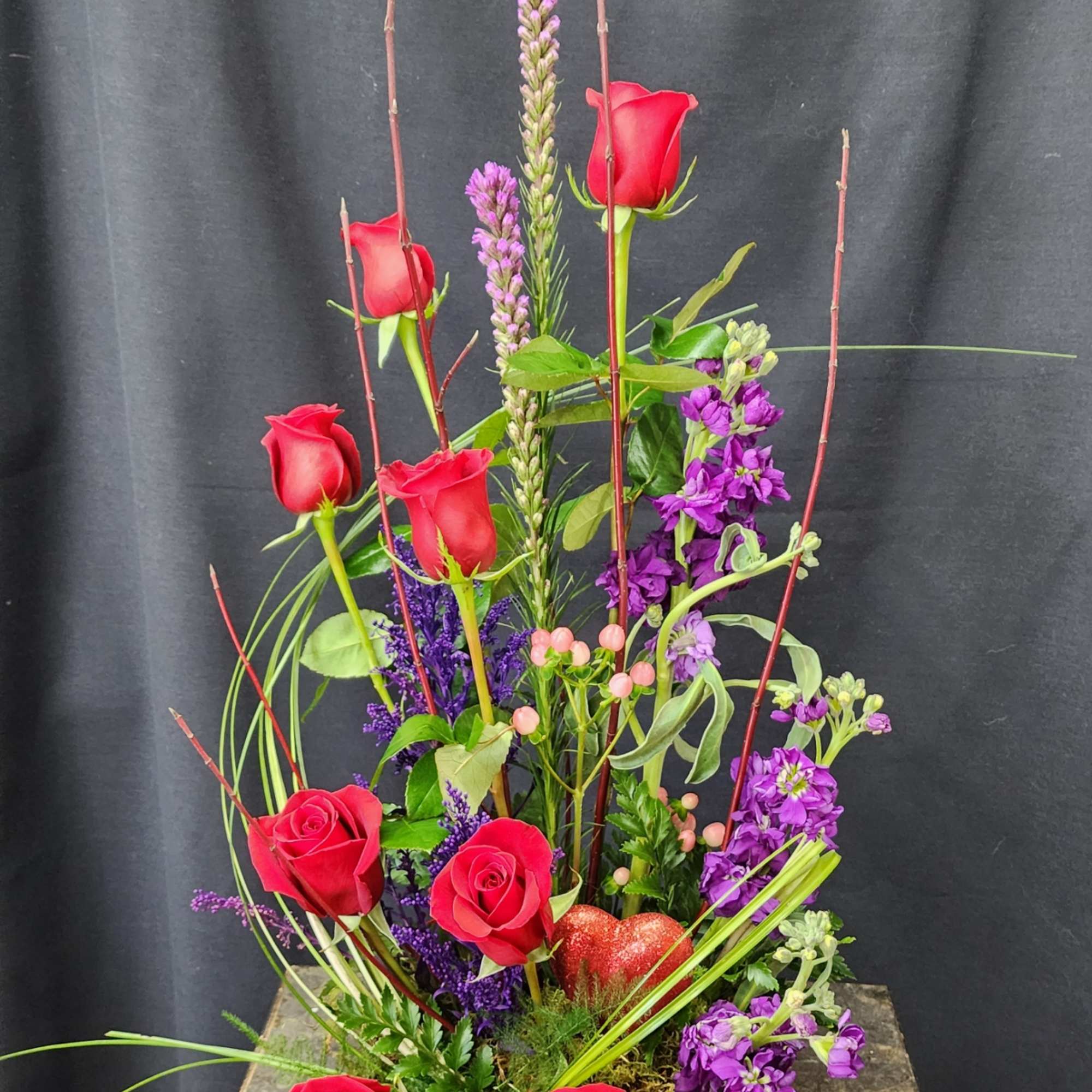 Tall arrangement of red roses and purple flowers in a low black container