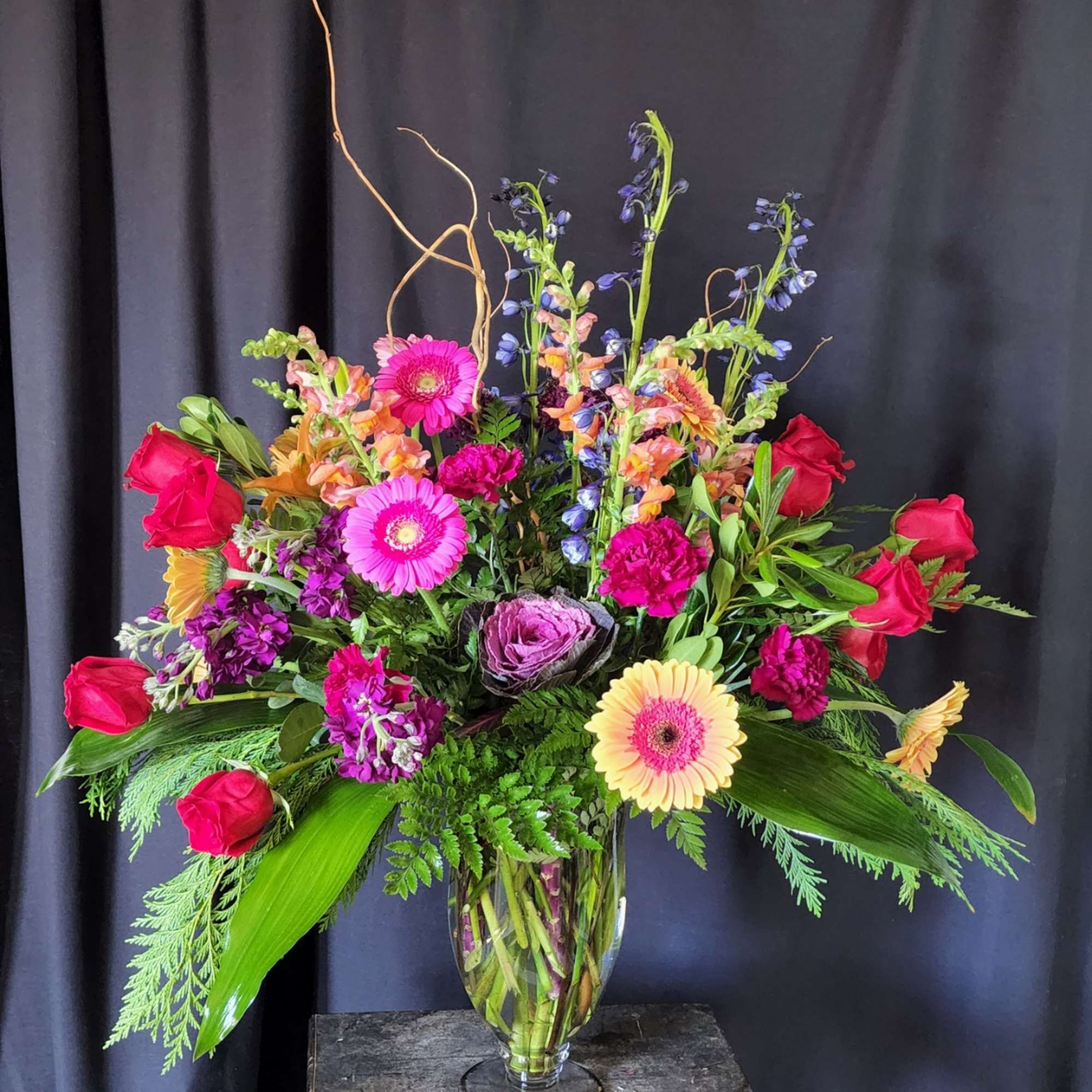 Tall mixed bouquet in a clear glass vase with red roses and bright gerbera daisies
