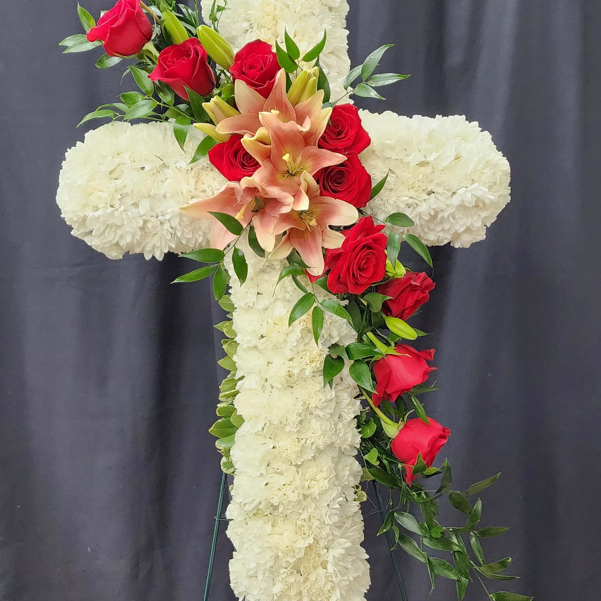 White floral cross with red roses and peach lilies on a stand