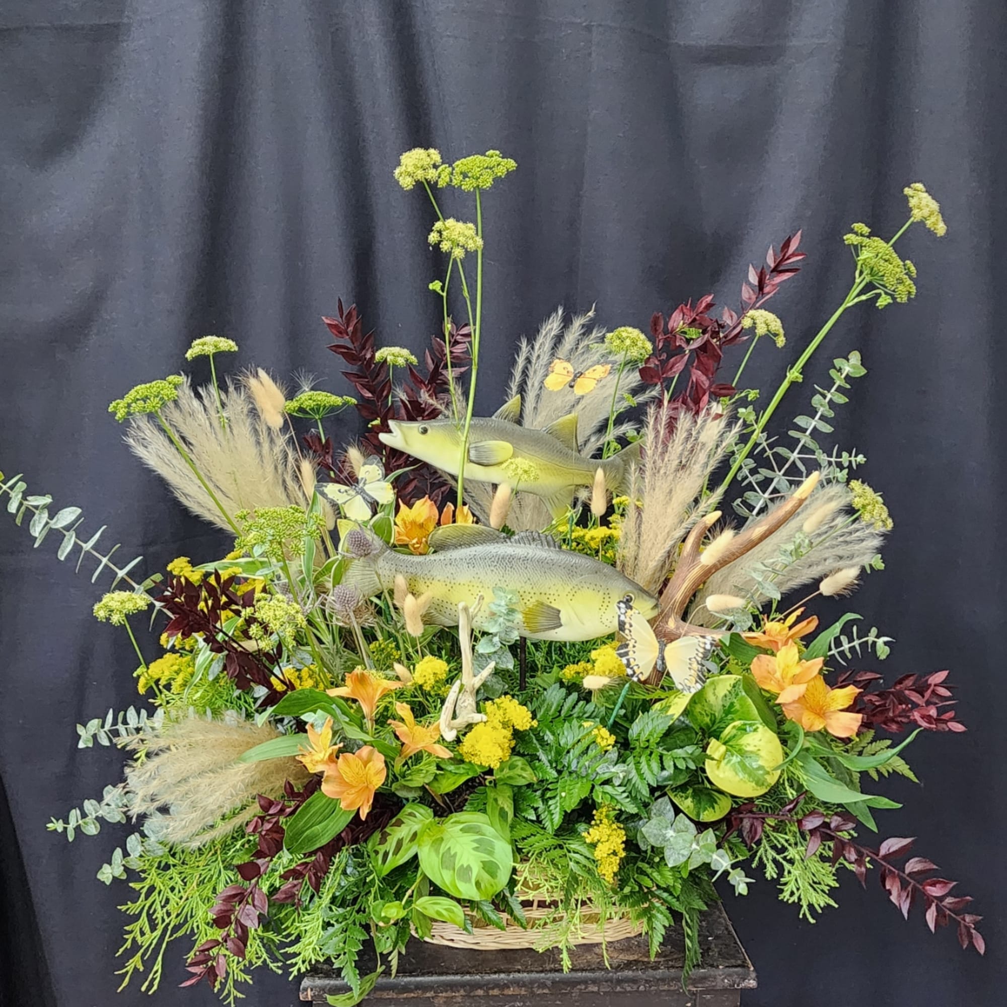 Basket arrangement with fish figures, orange flowers, and mixed greenery