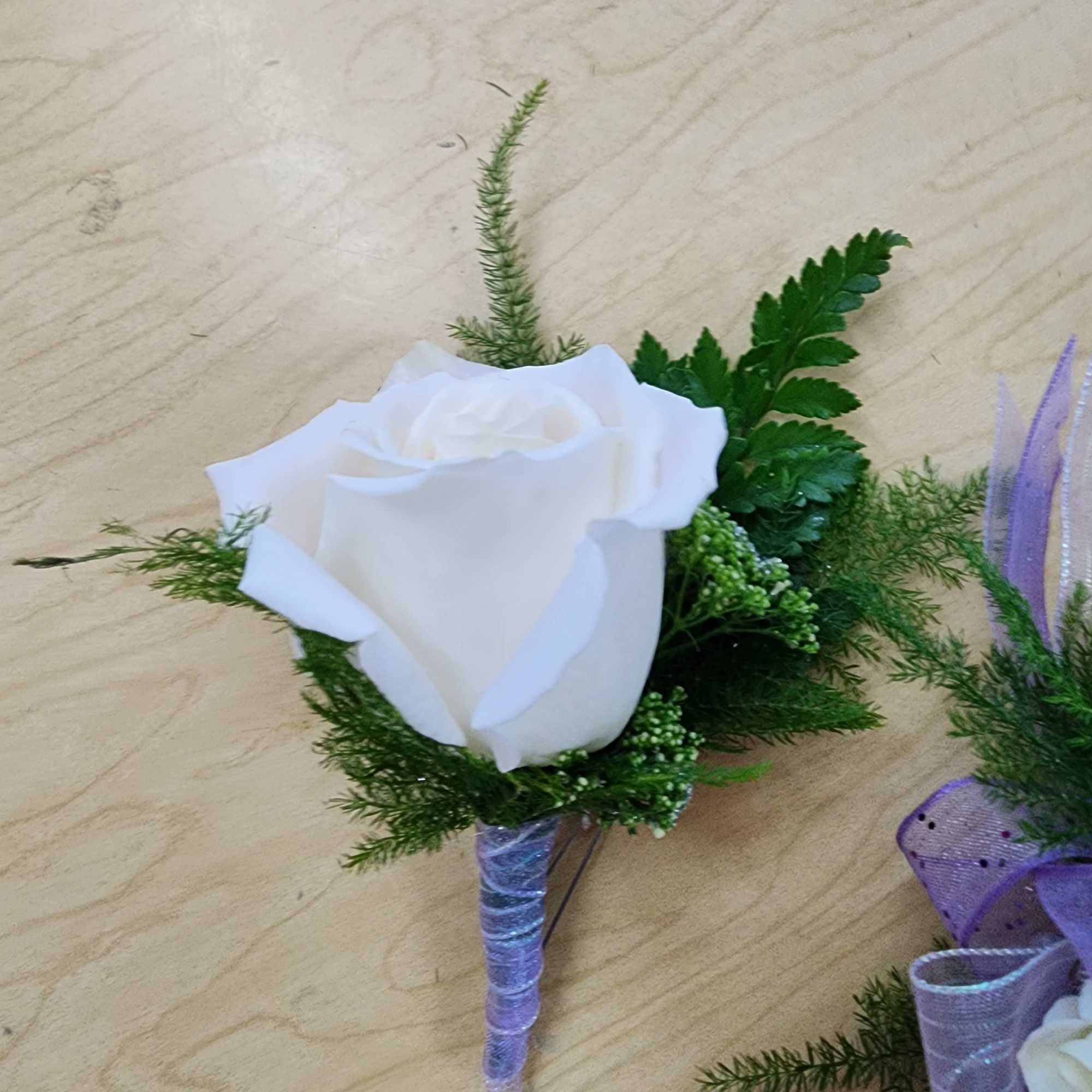 White rose boutonniere with green foliage and a purple wrapped stem