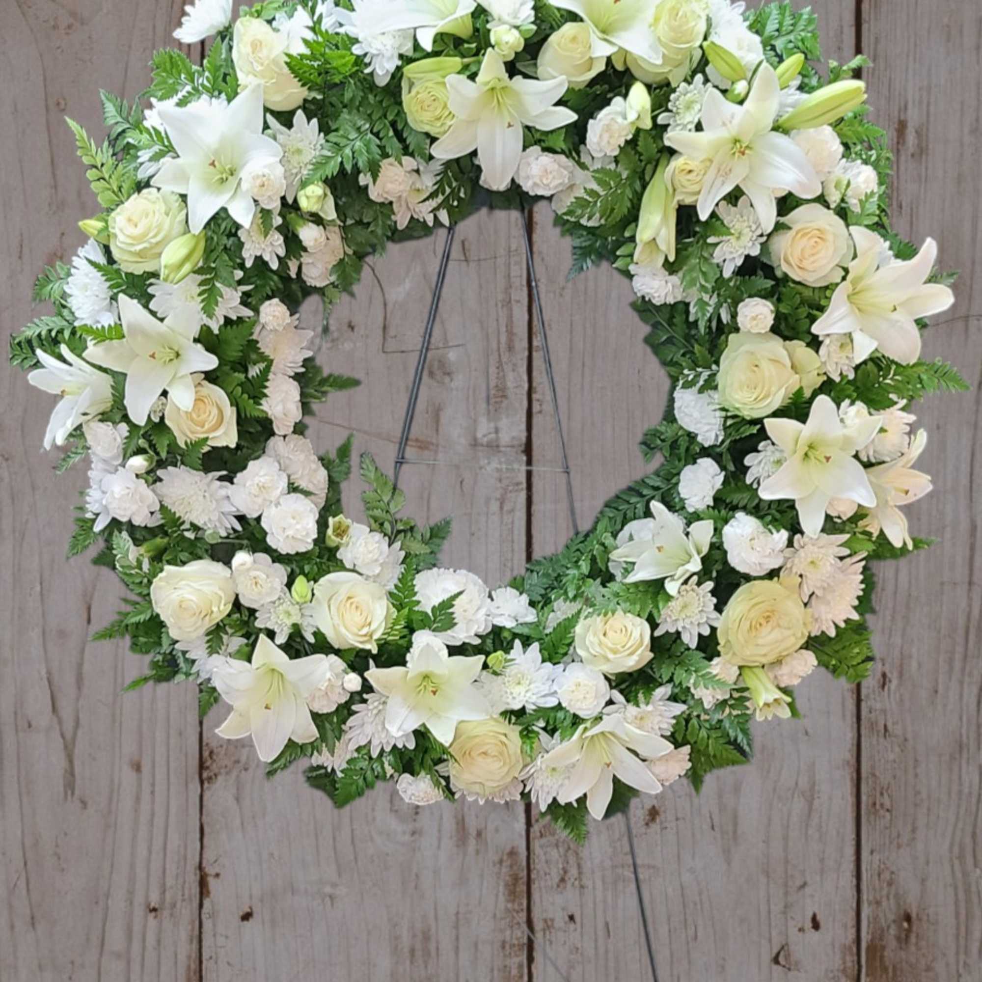 White floral wreath on a metal stand against a wood backdrop