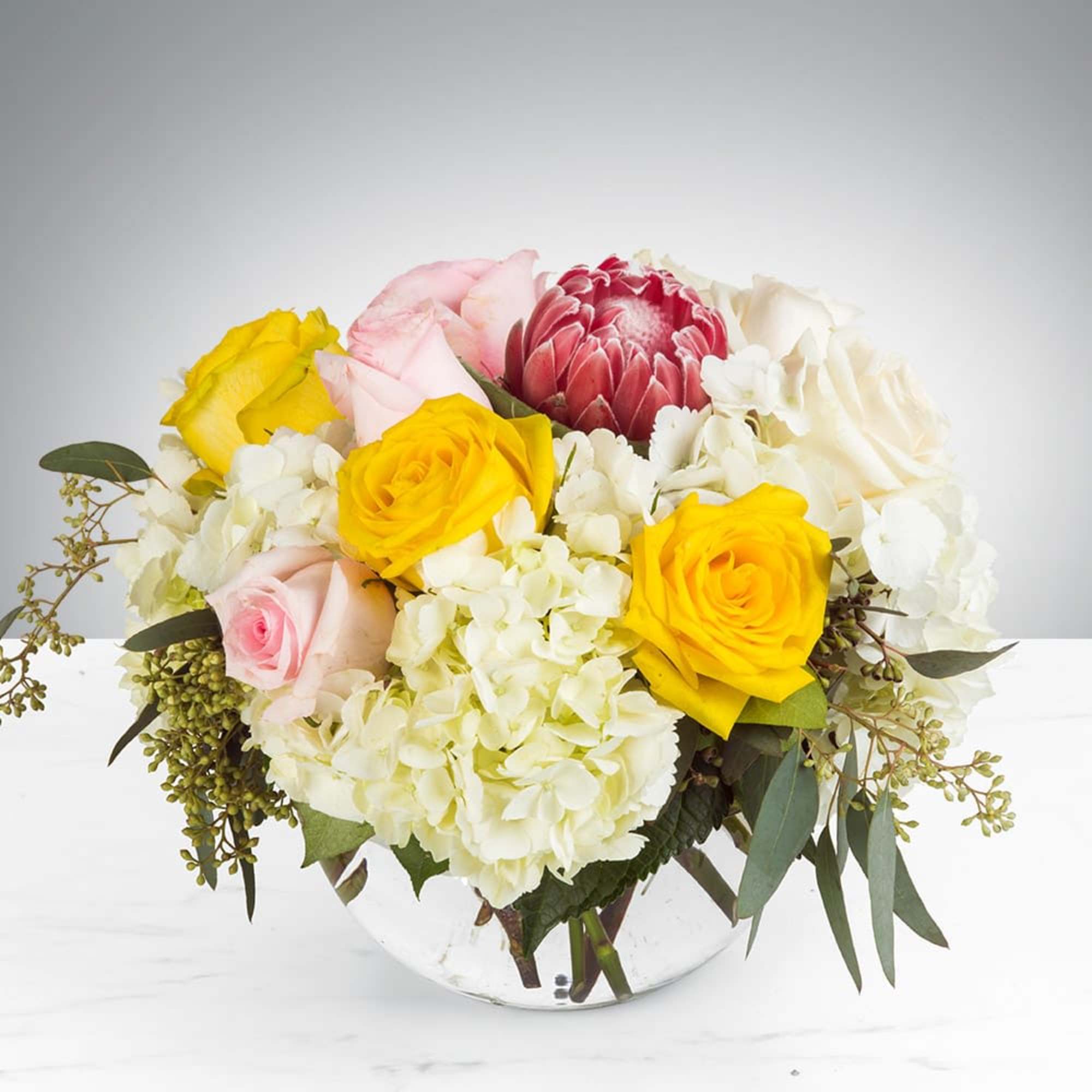 Bouquet of yellow, pink, white, and red flowers in a clear glass bowl vase