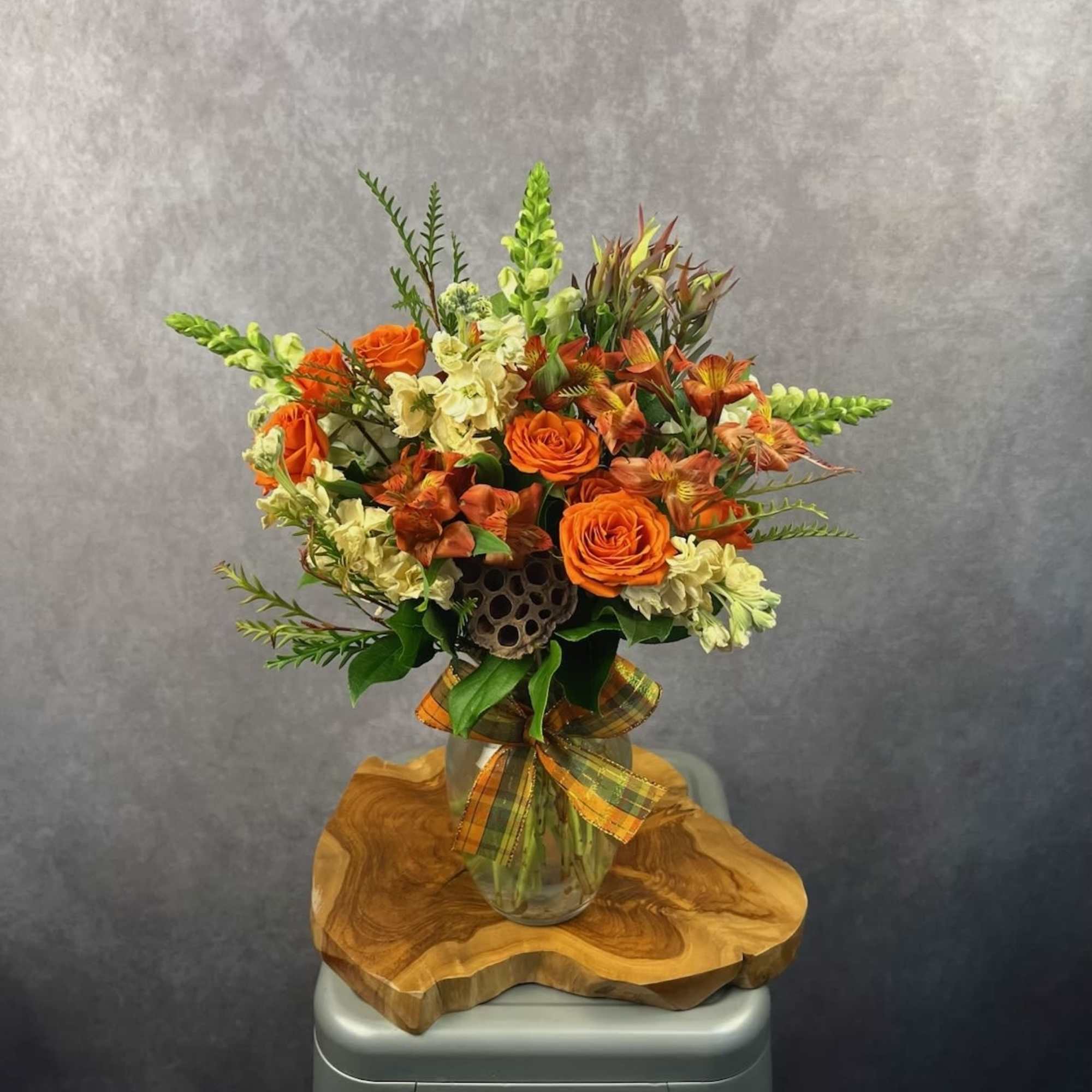 Orange roses and pale snapdragons in a glass vase with a plaid ribbon