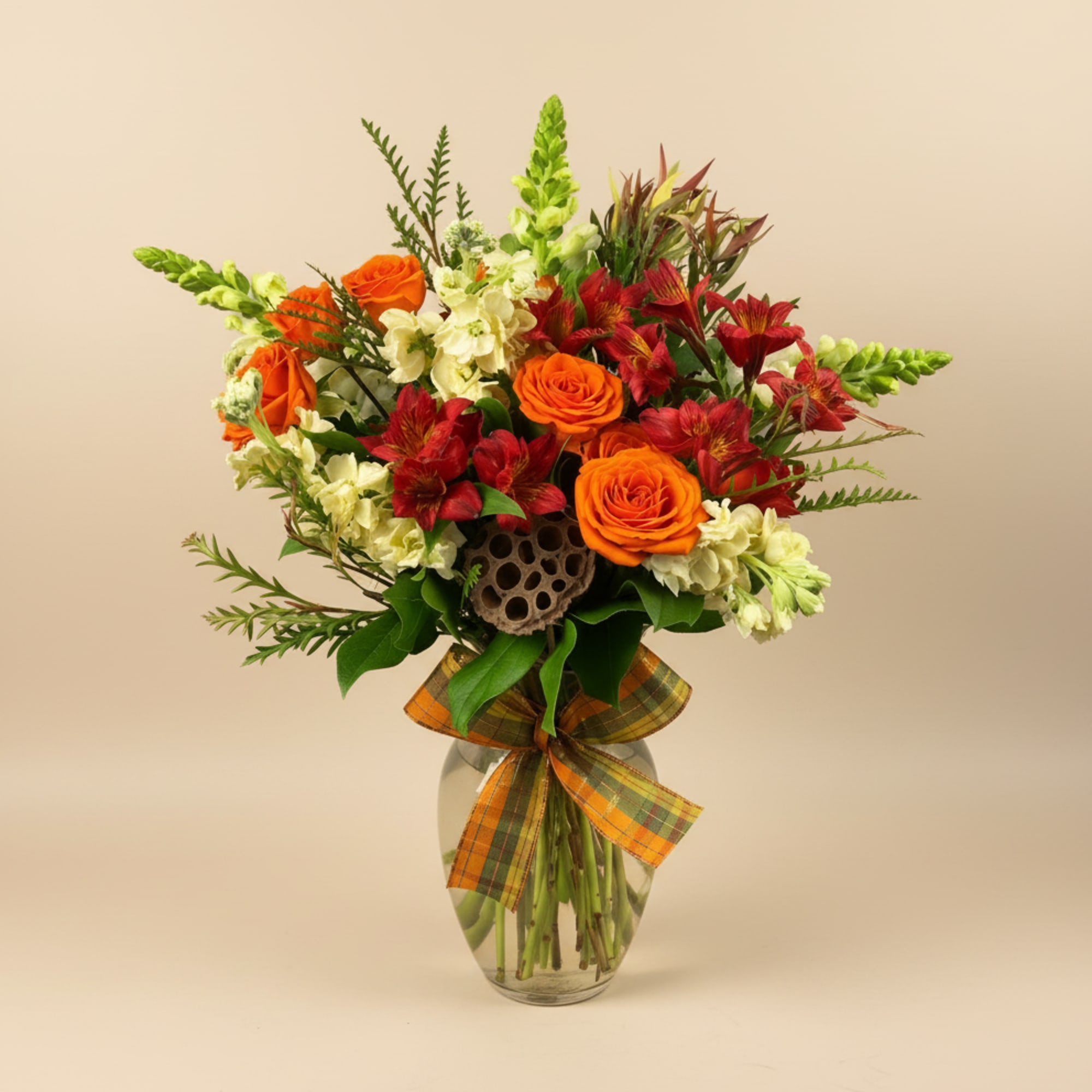 Orange roses and red alstroemeria in a glass vase with a plaid ribbon