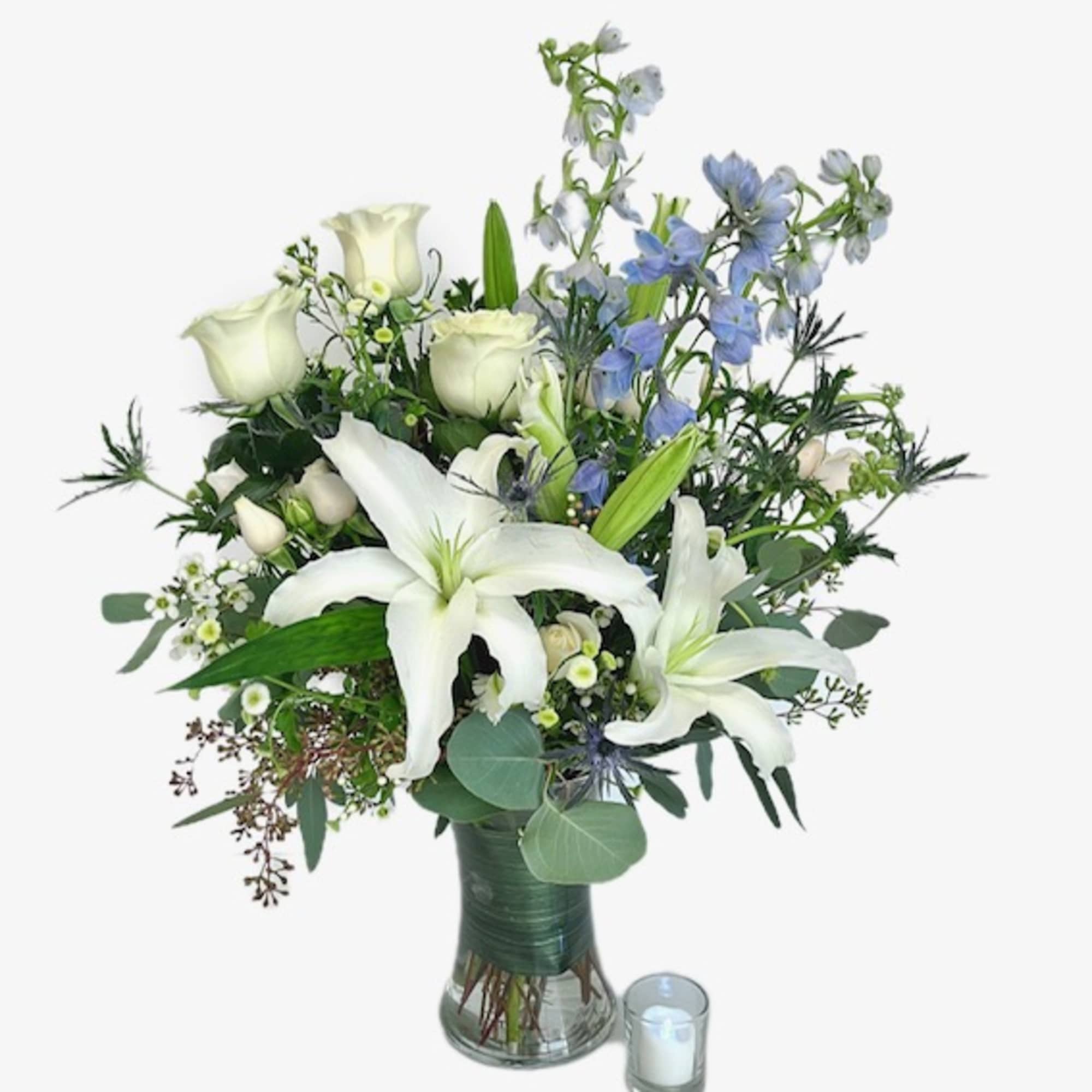 White lilies and roses in a glass vase with a small candle beside it